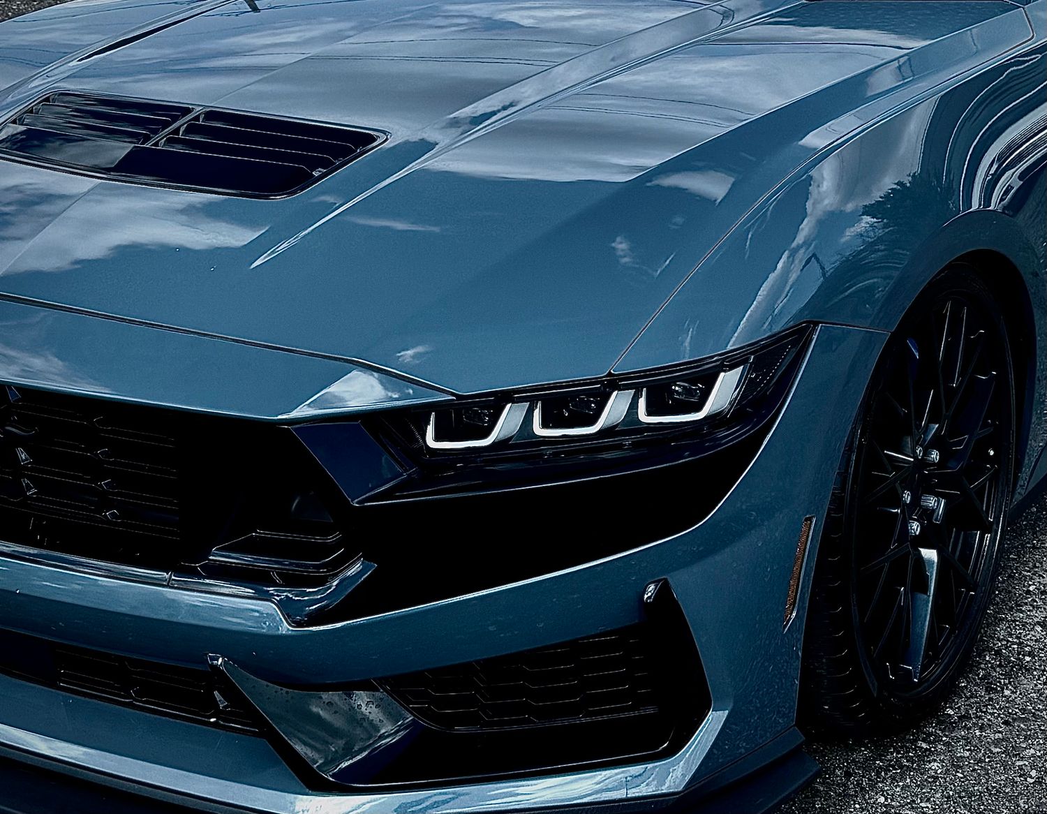 Close-up of a sleek dark blue Ford Mustang featuring aggressive LED headlights and sculpted hood design.