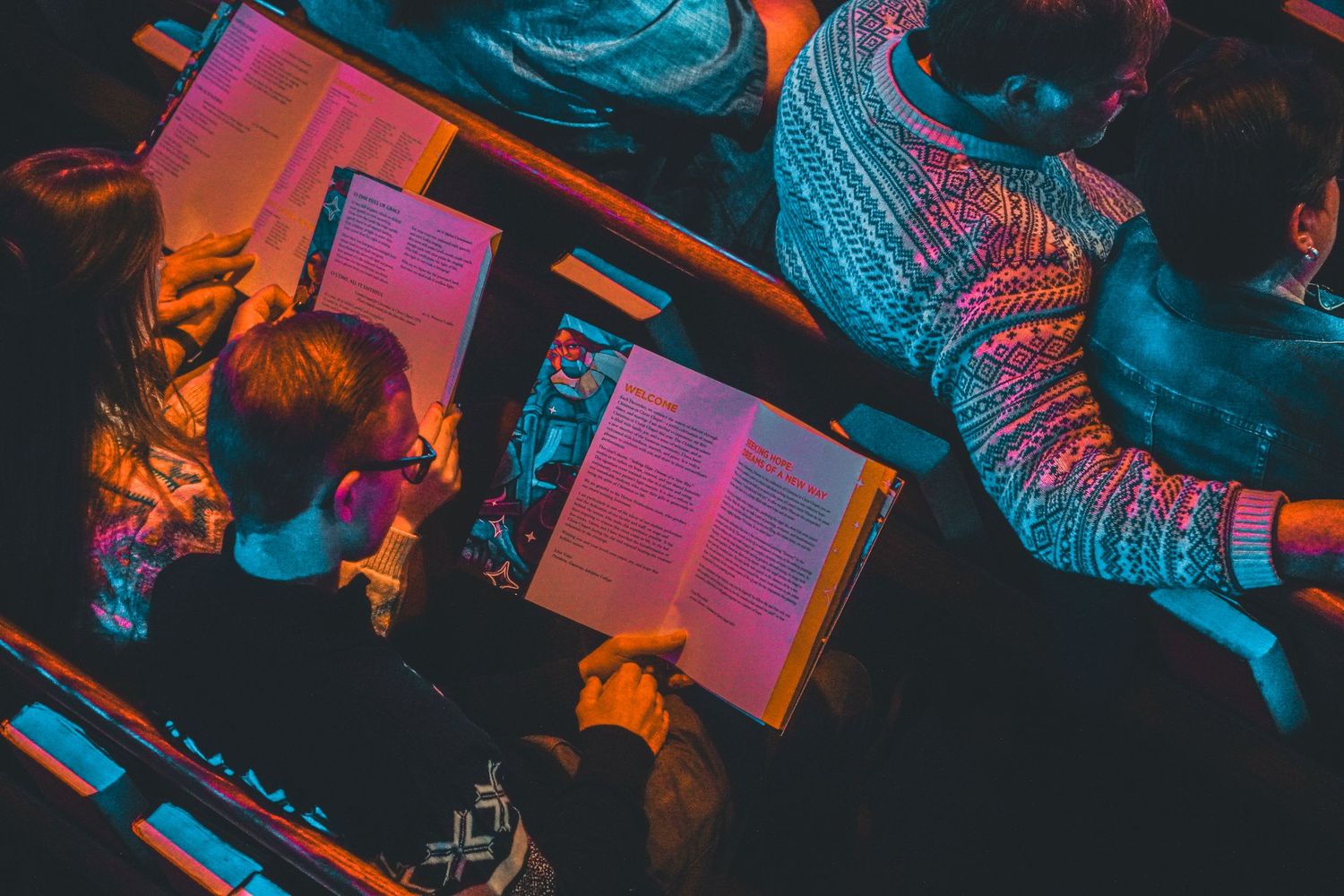 People reading books under colorful neon lighting creating a moody atmospheric scene.