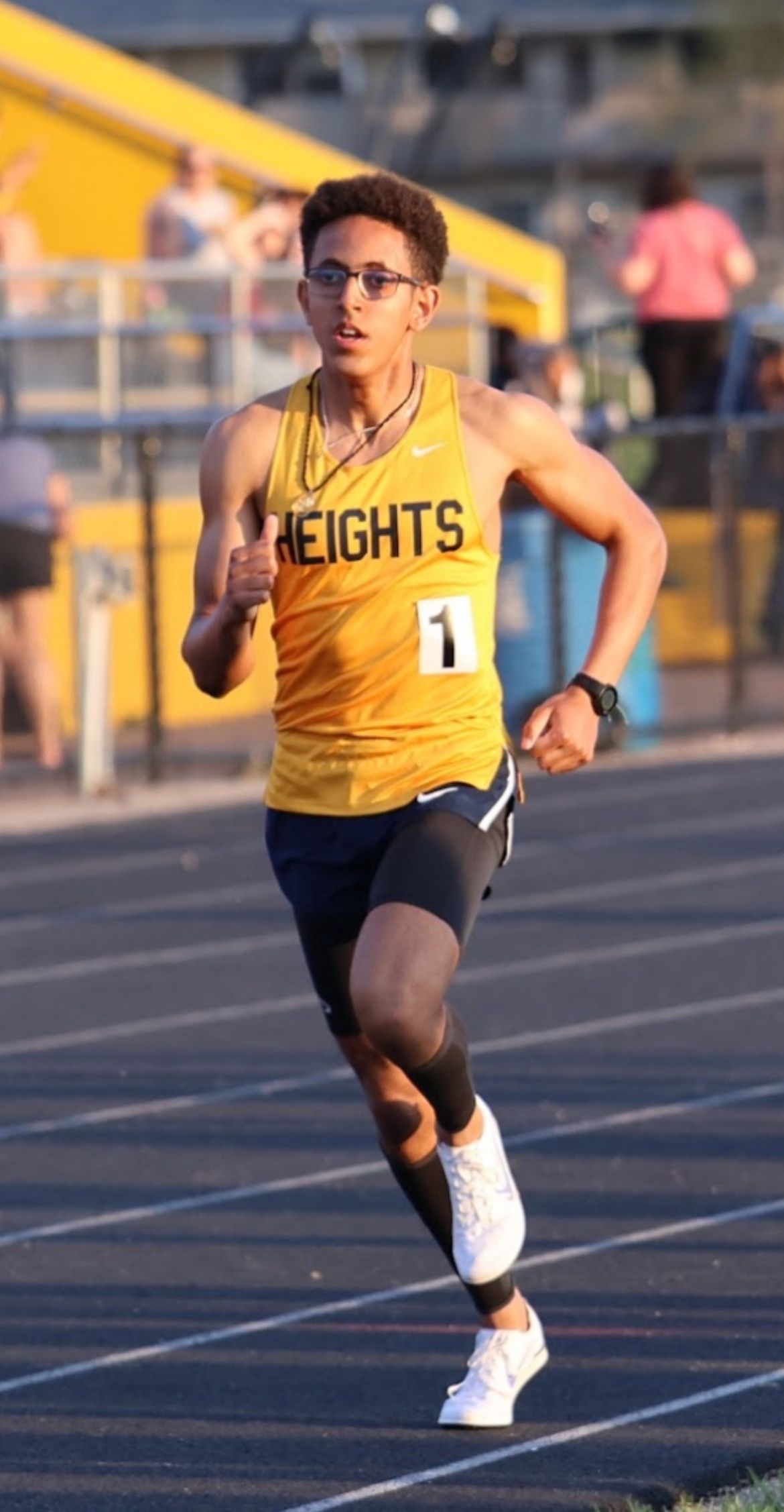 Track athlete in a yellow uniform sprinting on an outdoor track during competition.