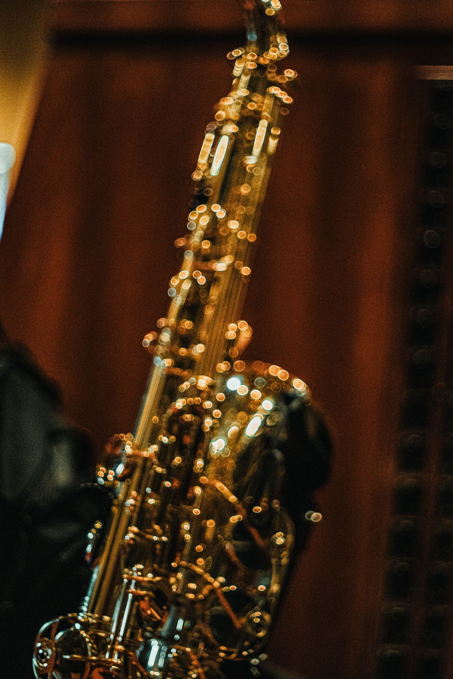 Close-up of a gleaming gold alto saxophone with bokeh light reflections against a warm brown background.