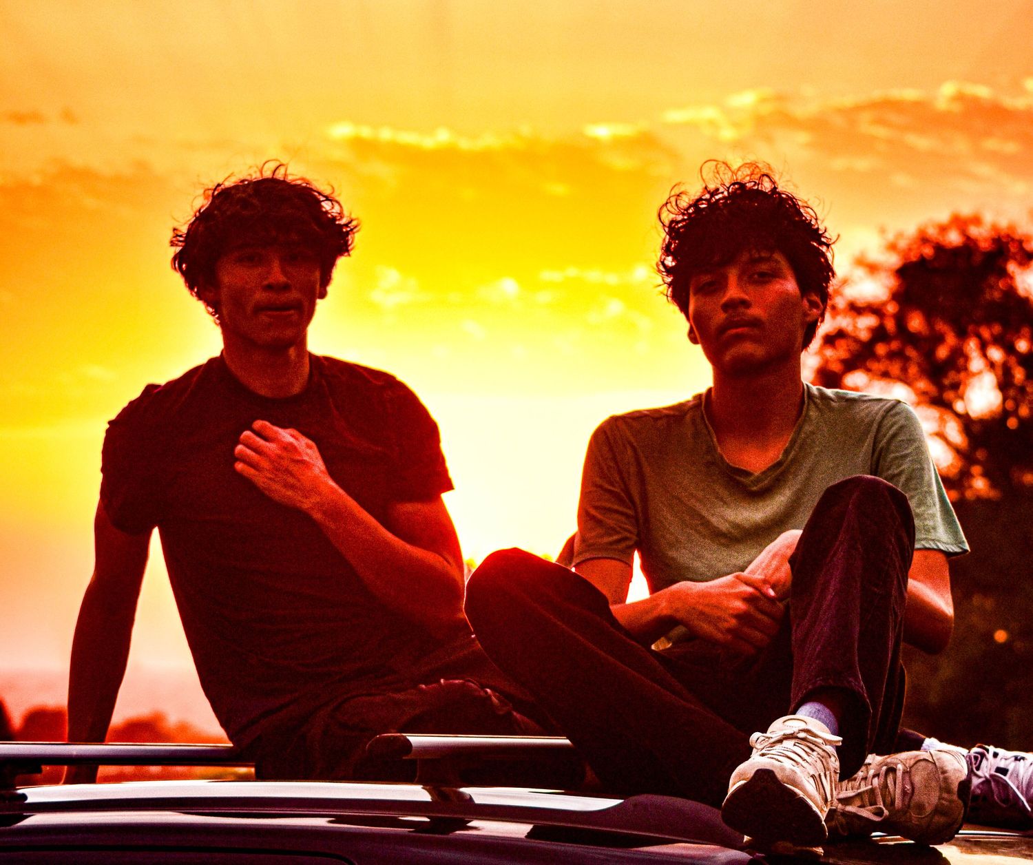 Silhouettes of people sitting together on a car against a vibrant orange and yellow sunset sky.