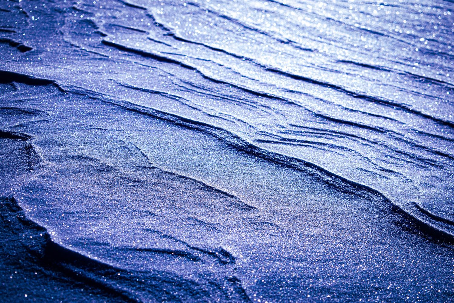 Abstract pattern of sparkly snow and wave-like patterns on the snow surface with textured detail.