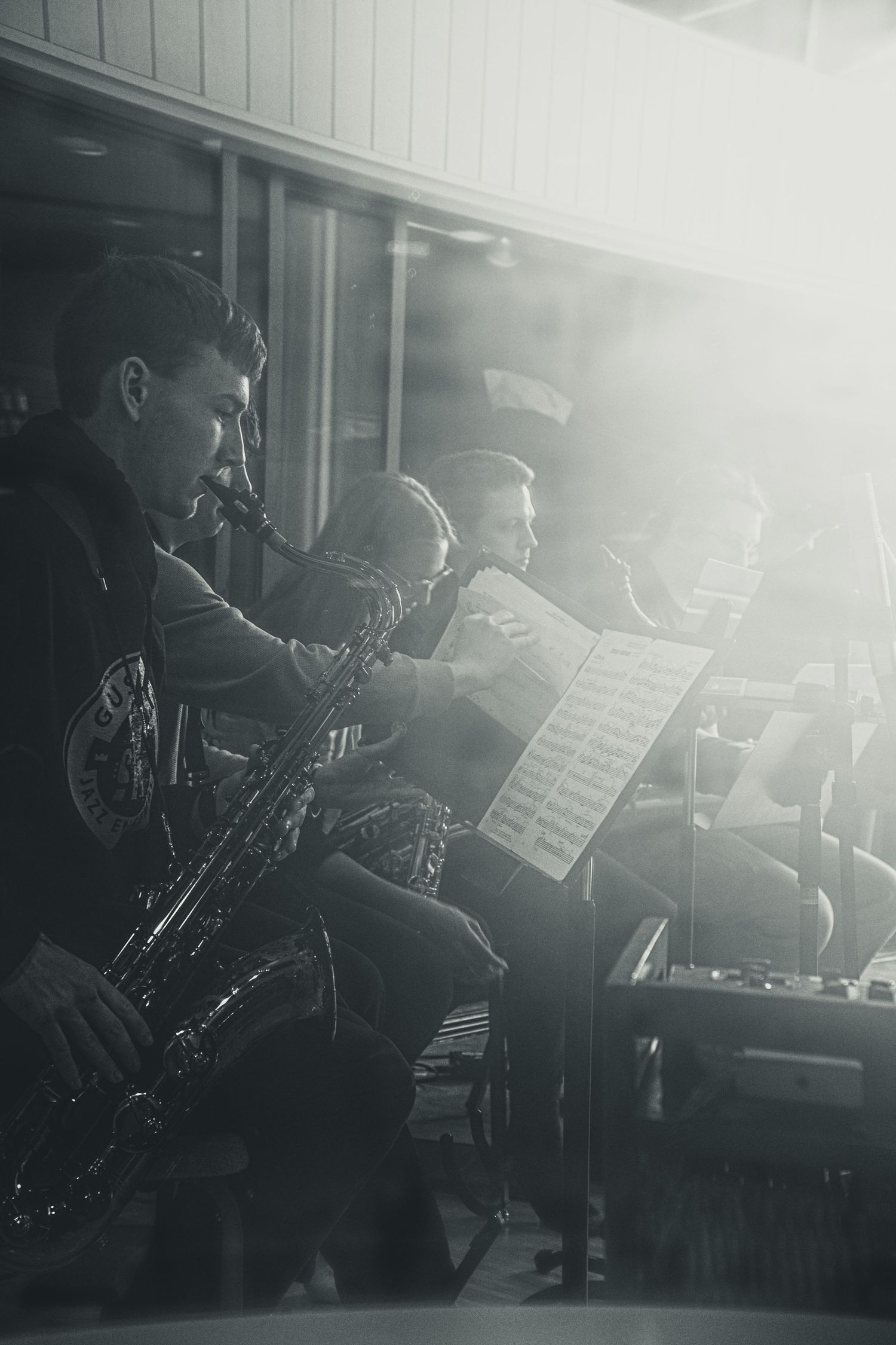Black and white photo of jazz musicians playing saxophones while reading sheet music during a live performance.