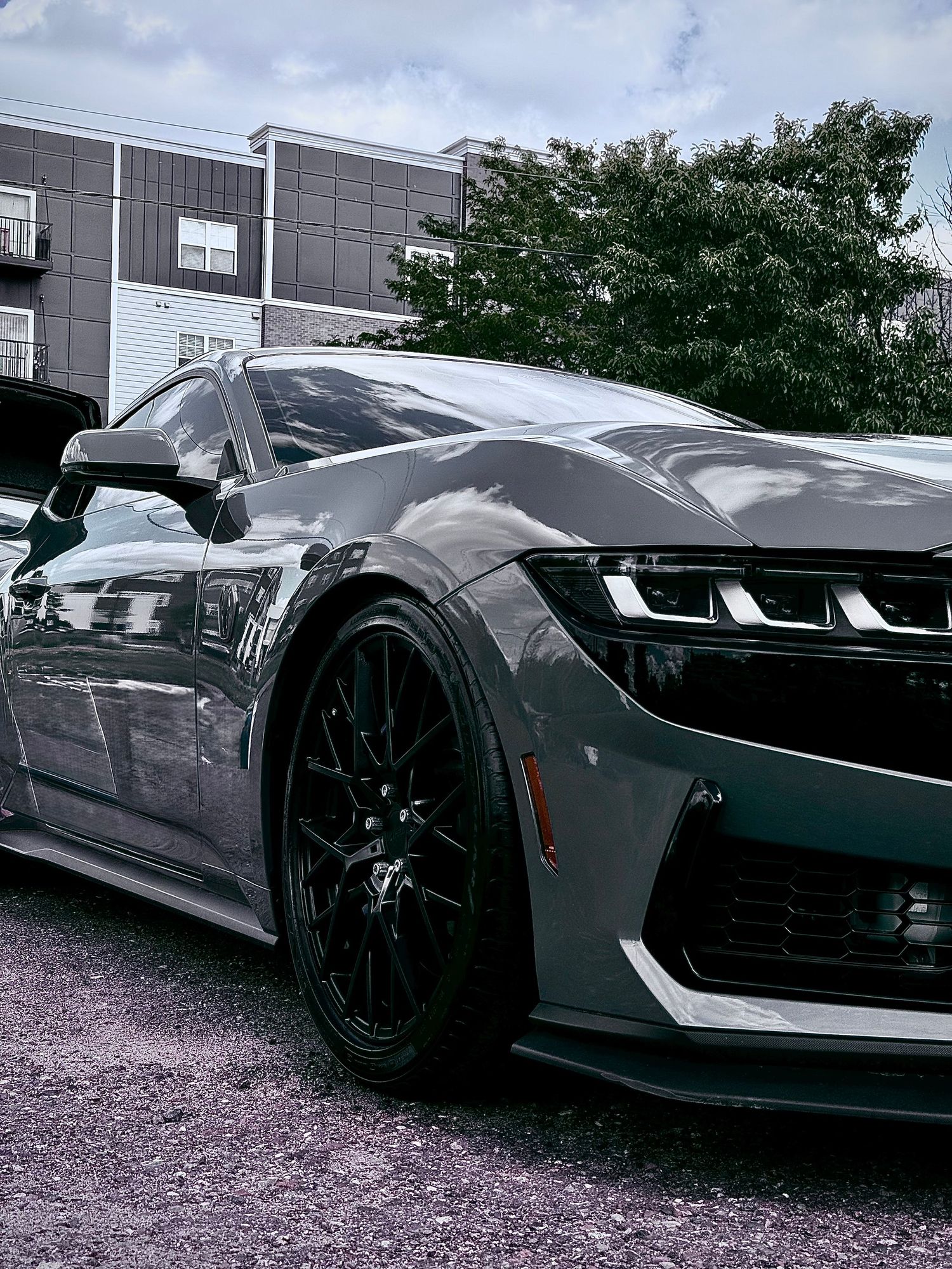 Dark gray Chevrolet Camaro with black rims parked in a lot, showcasing aggressive front end styling.