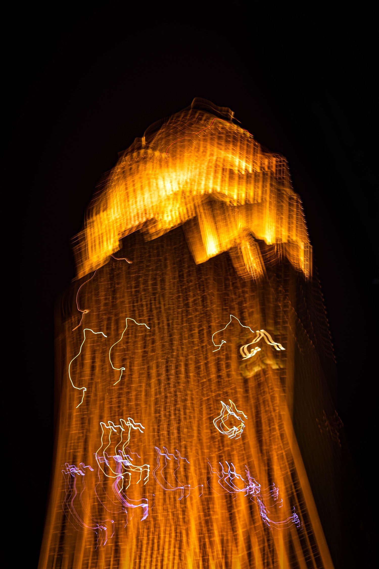 Illuminated tower with glowing orange light trails creating abstract patterns against night sky.