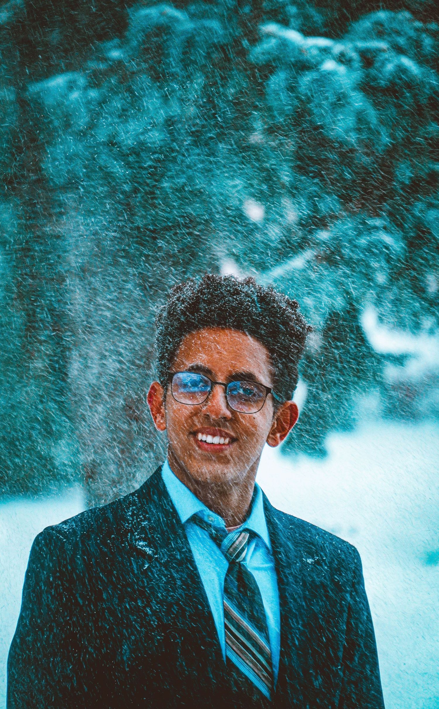 Portrait in blue tones shows a person in winter snow wearing glasses and a suit.