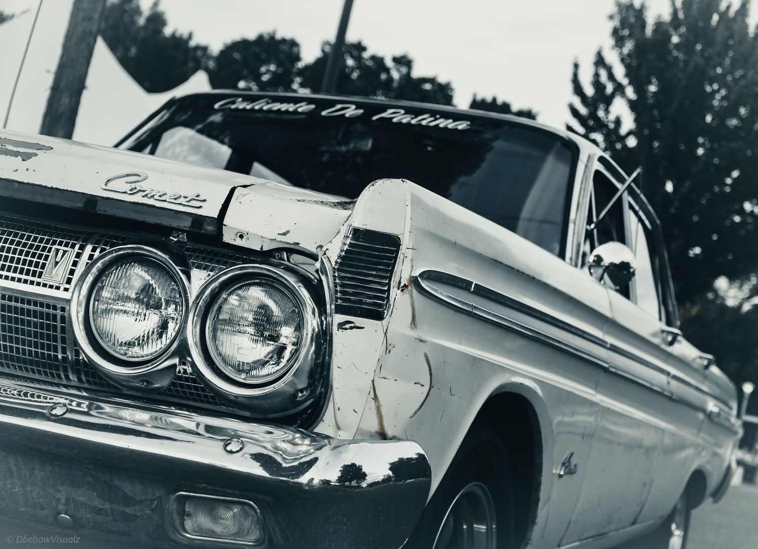Vintage black and white photo of a damaged classic car with dual headlights and custom windshield lettering.