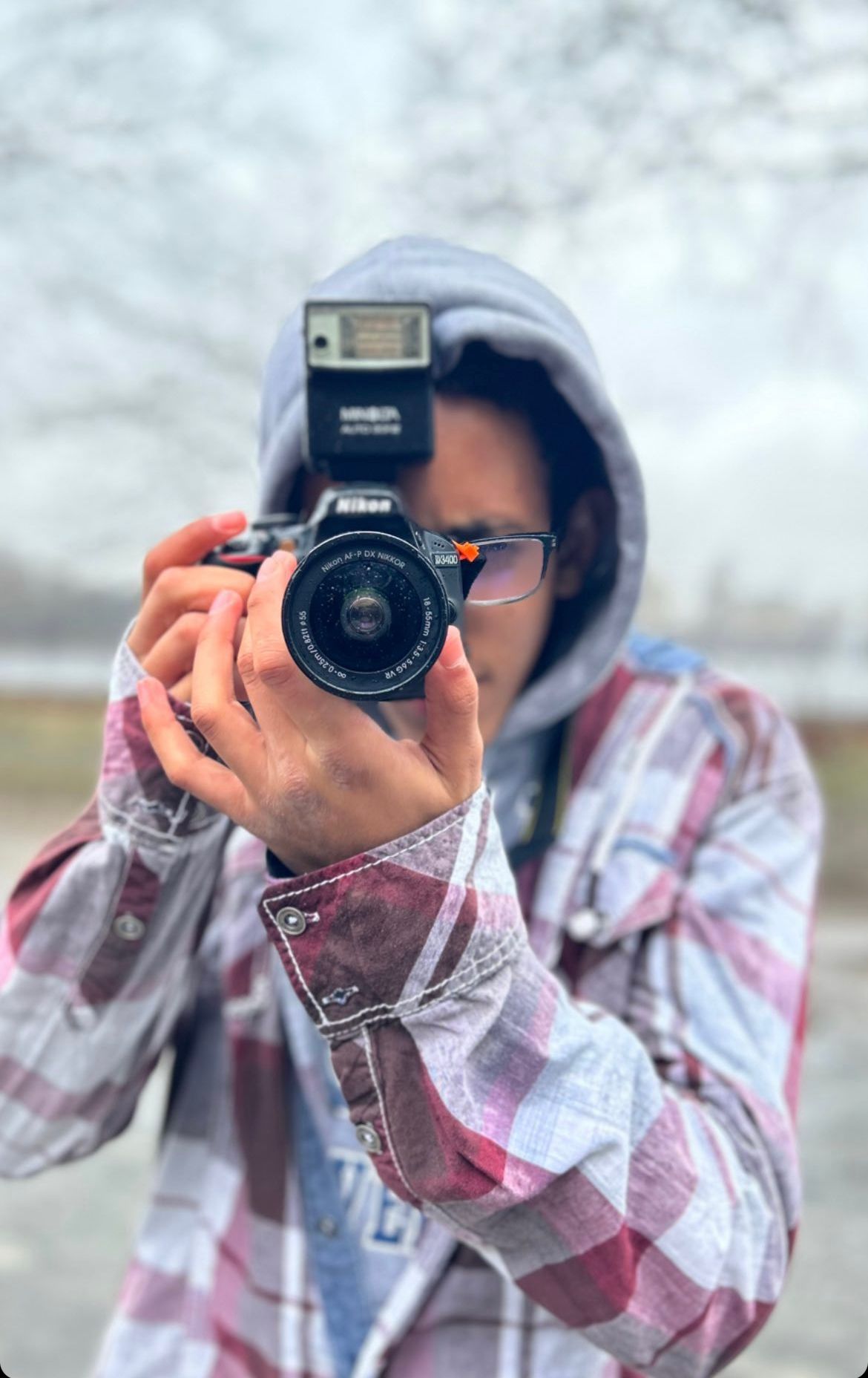 Photographer wearing a hoodie and plaid shirt taking a portrait with a vintage camera.