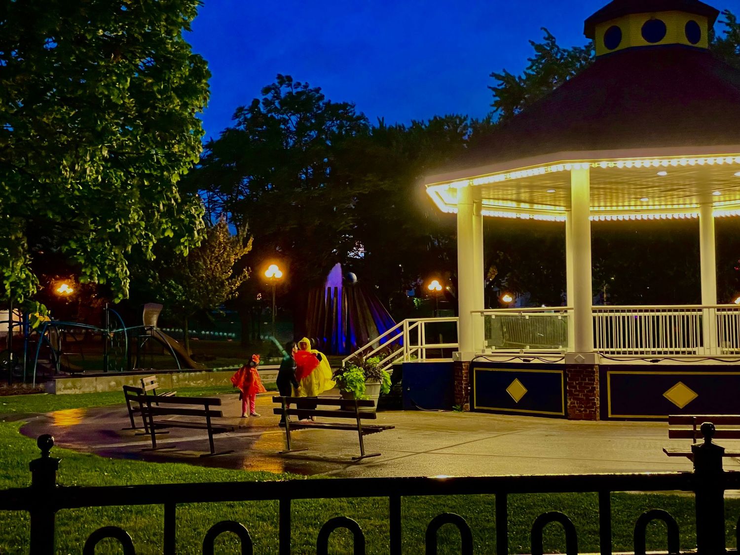 Night scene of illuminated park pavilion with playground equipment visible in background.