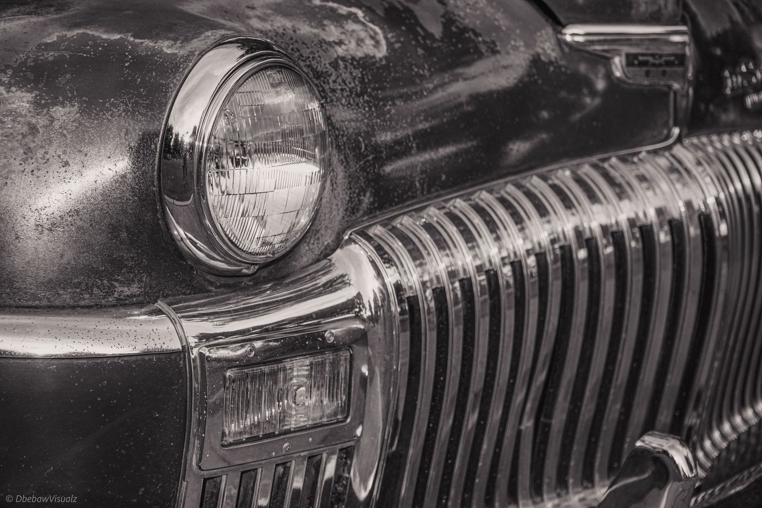 Black and white close-up of a vintage car headlight and chrome grille, showcasing classic automotive design.