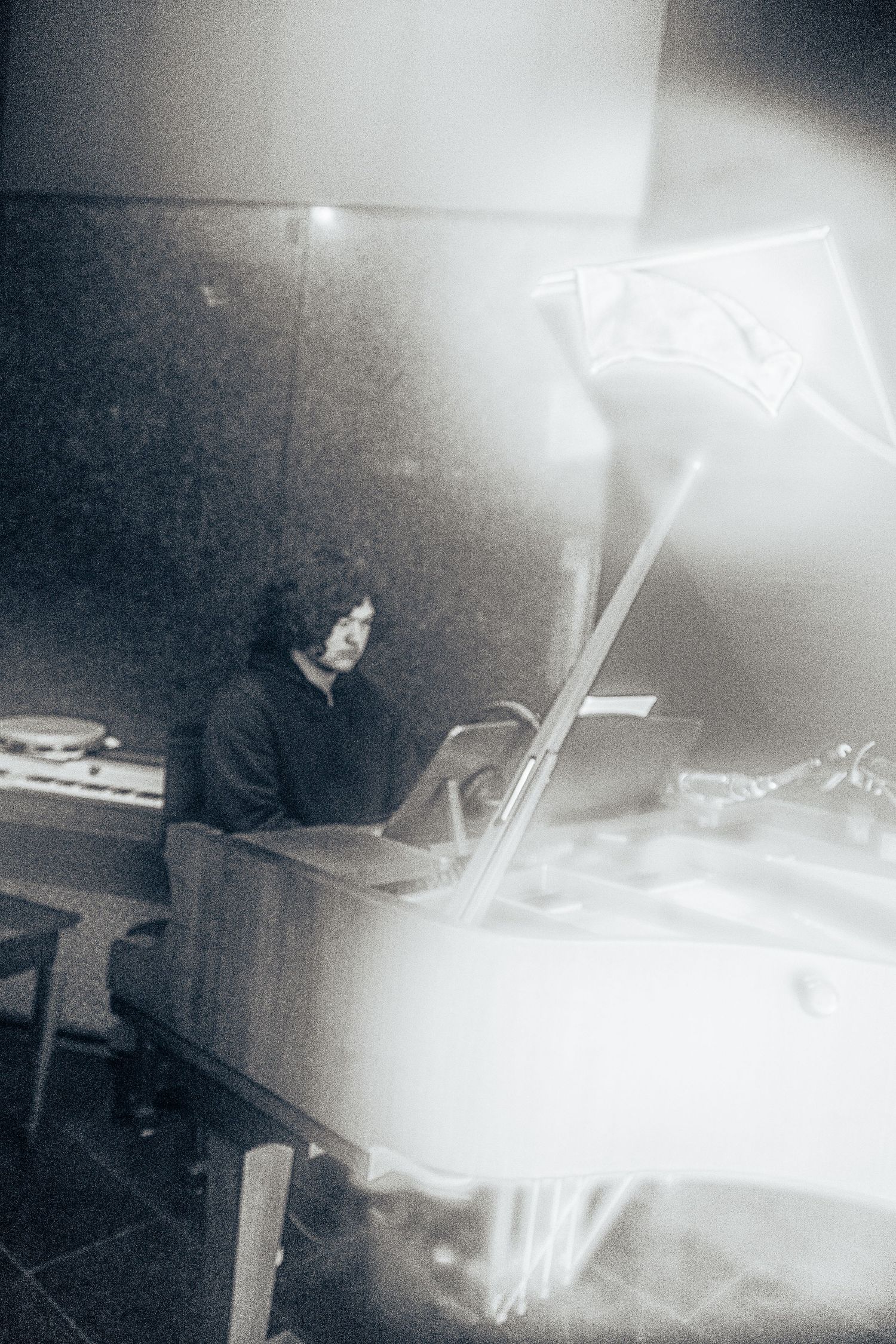 Black and white photo of a person sitting at a piano in a dimly lit room with a light flare effect.