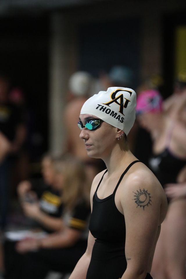 Swimmers line up at the edge of the pool wearing competition swim caps and goggles.