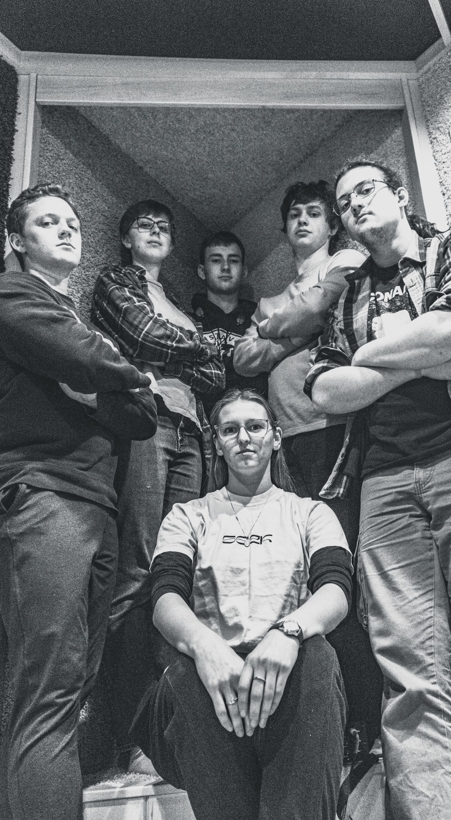 Black and white photo of six young people posing dramatically in a doorway, looking down at camera.