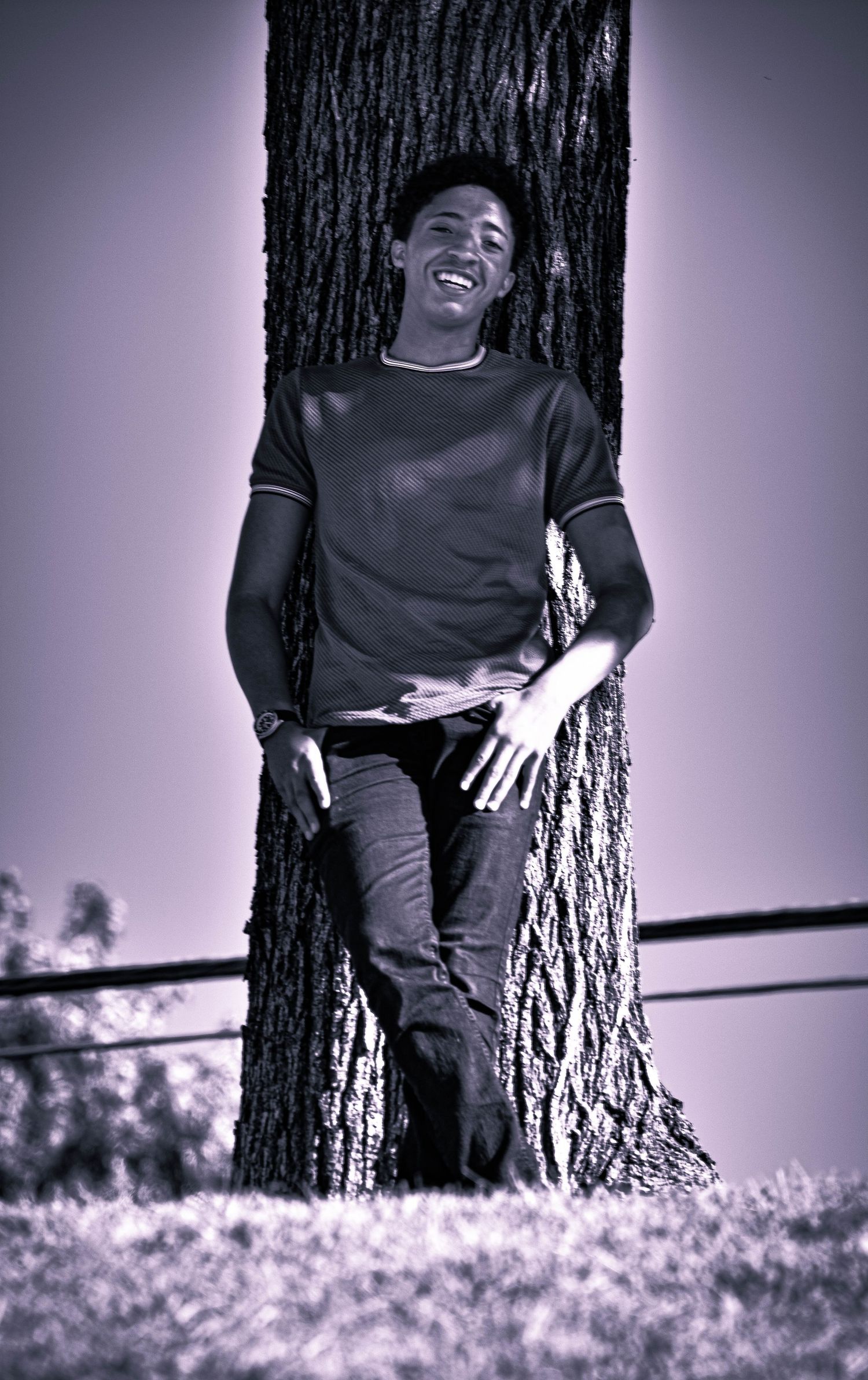 A person relaxing against a large tree trunk in black and white photography.