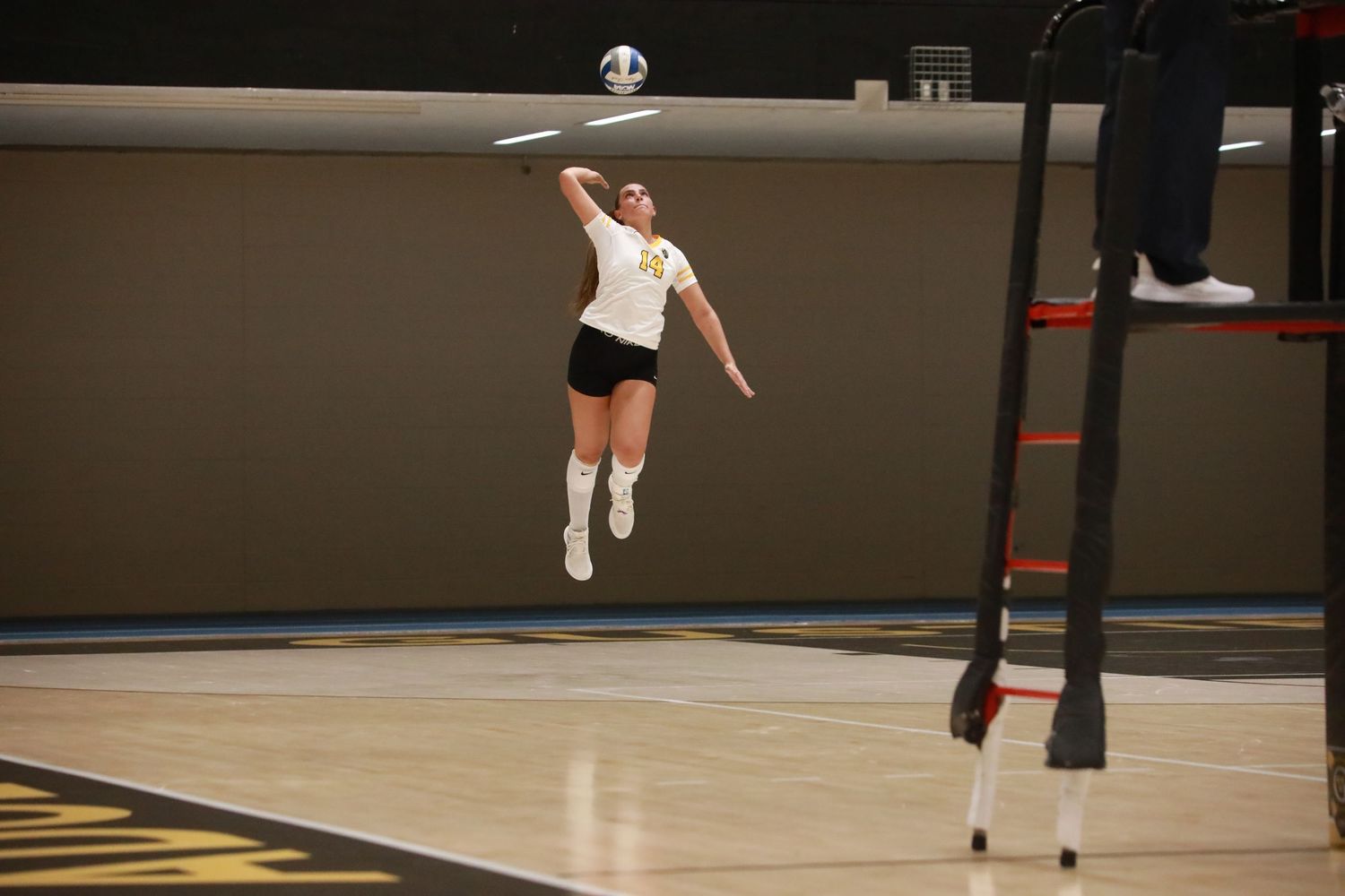 Volleyball player leaps high to spike ball during indoor match.