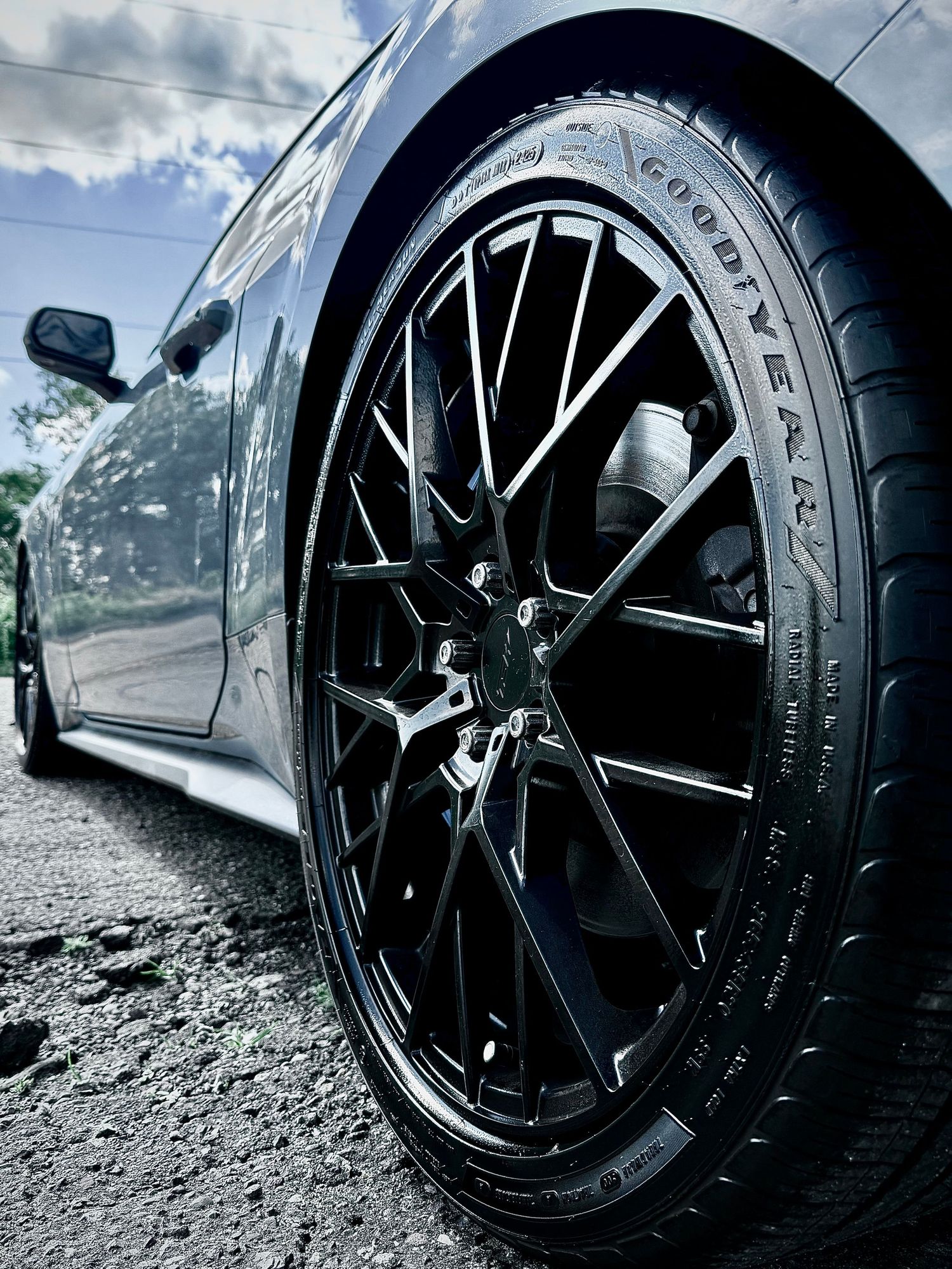 Close-up of a black Goodyear tire on a sleek multi-spoke black alloy wheel on a dark gray sports car.