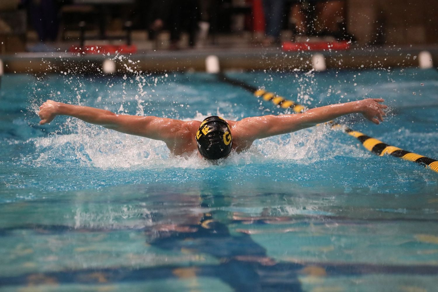 Swimmer performs butterfly stroke during competition with water splashing dramatically.