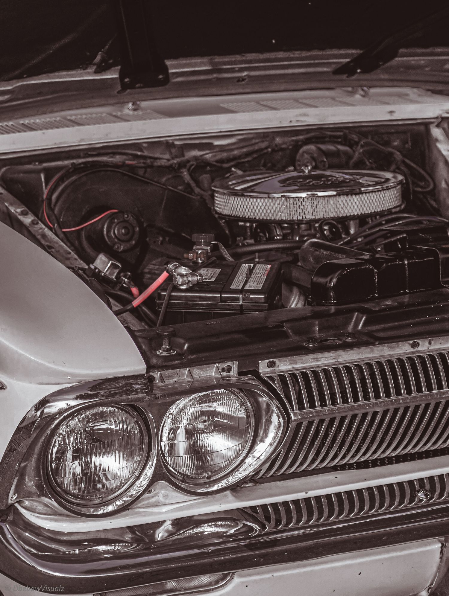 Vintage car with open hood revealing a classic V8 engine, chrome air filter, and red battery cables in sepia tone.