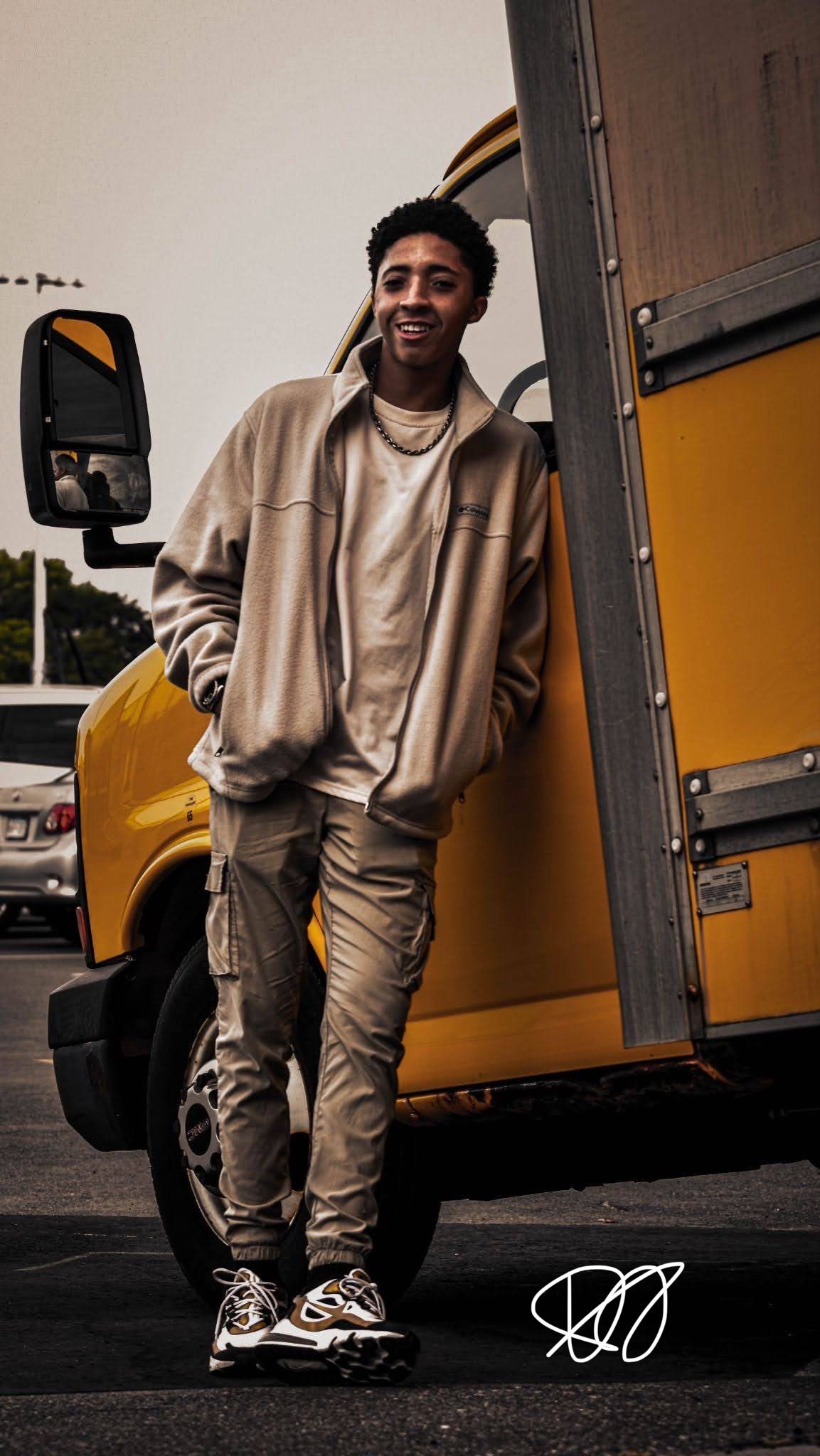 Person in casual beige outfit posing next to yellow delivery truck.