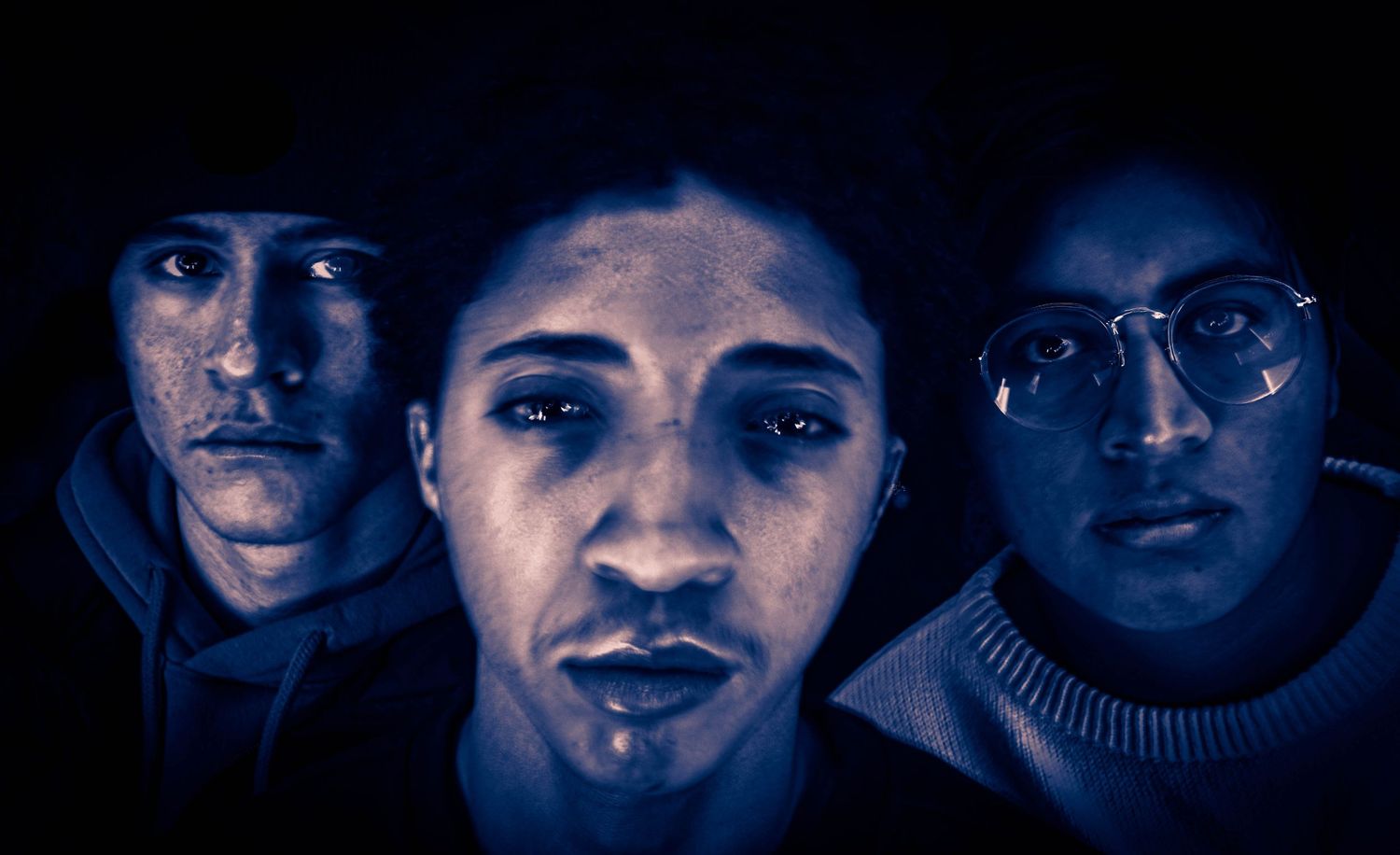 Three figures illuminated in dramatic blue lighting creating a moody portrait.