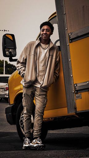 Person in beige sweatsuit posing casually next to yellow school bus.