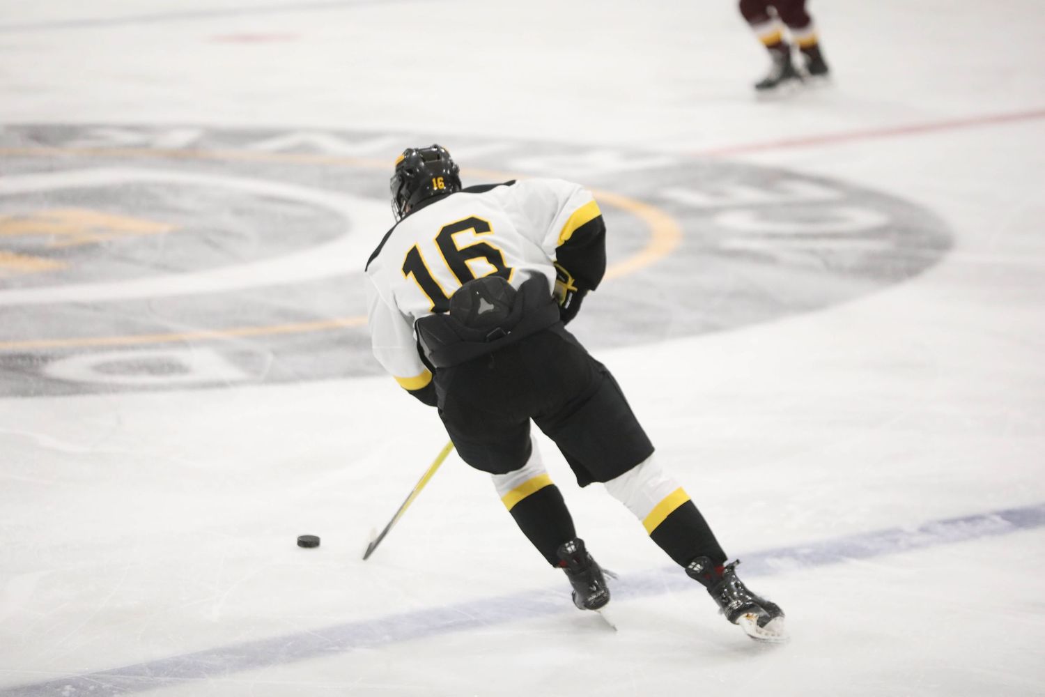 Hockey players skate across the ice during an intense game, with one player controlling the puck.