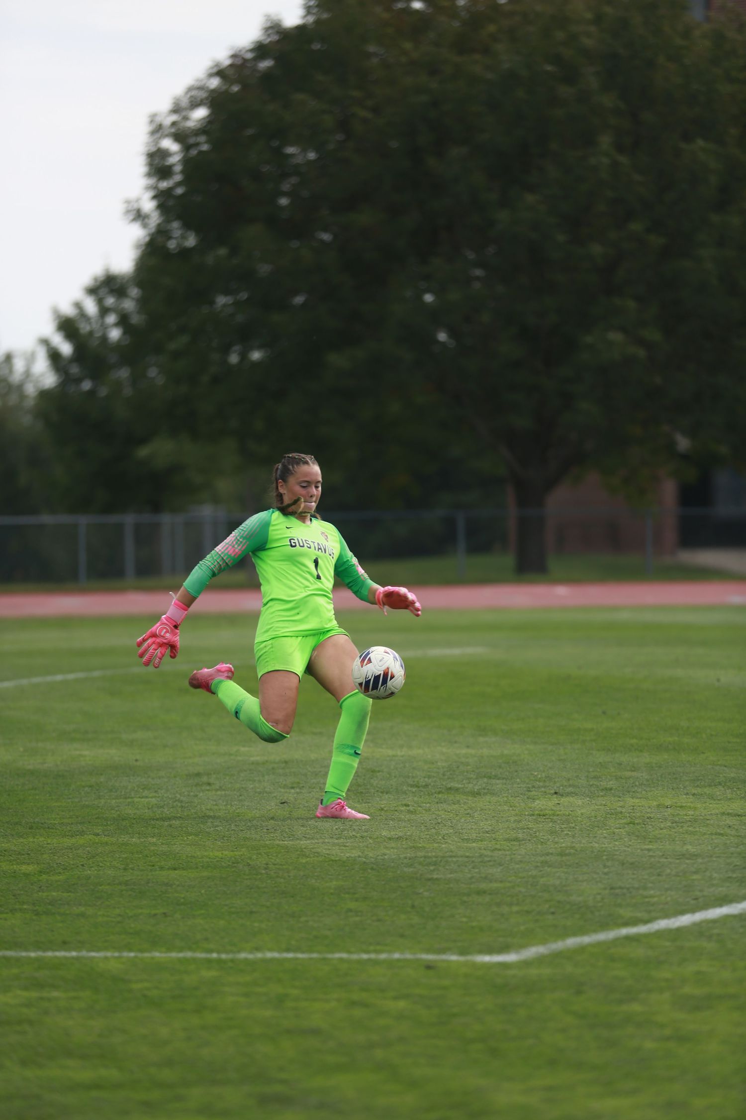A soccer goalkeeper in a bright green uniform makes a goal kick on a grass field.