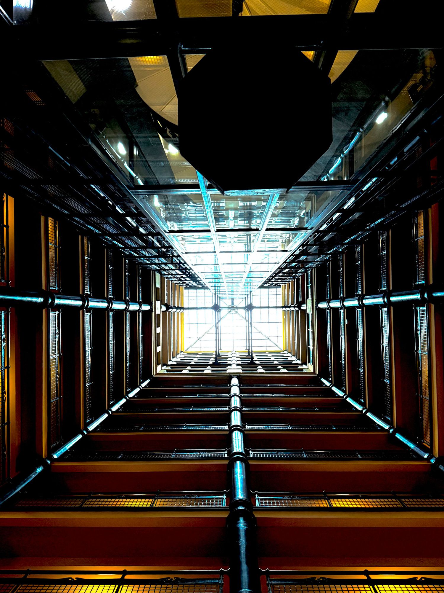 Looking up through a modern glass elevator shaft with glowing blue lights and geometric metal framework.