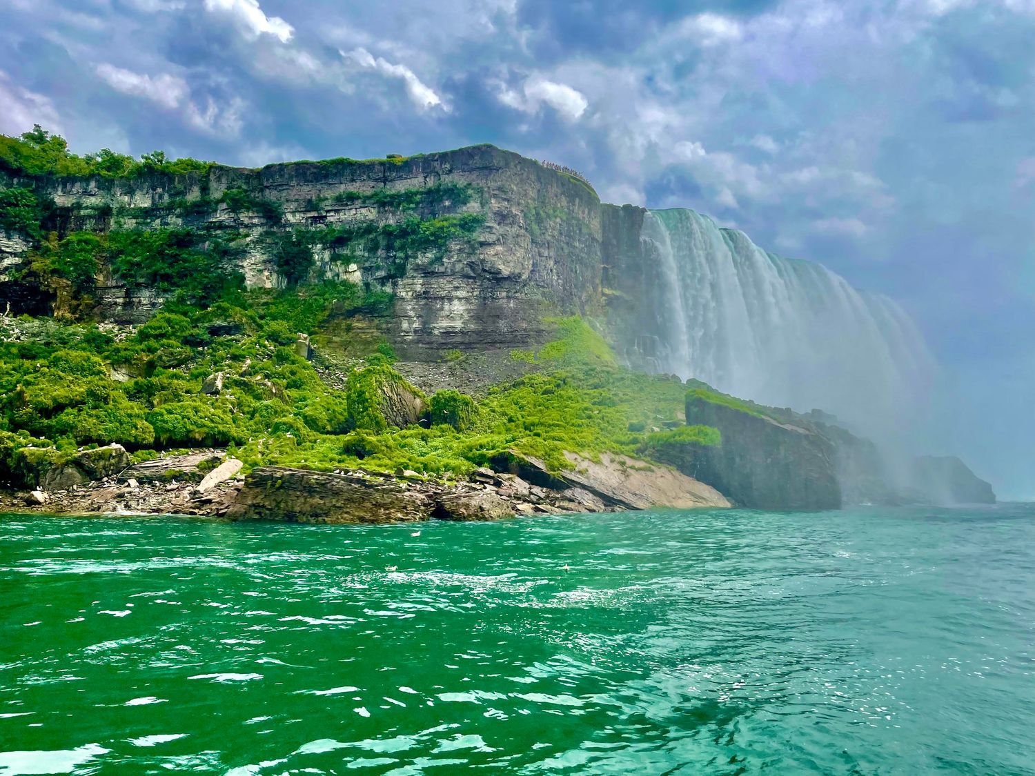 Niagara Falls cascading down rocky cliffs with lush greenery and turquoise waters below.
