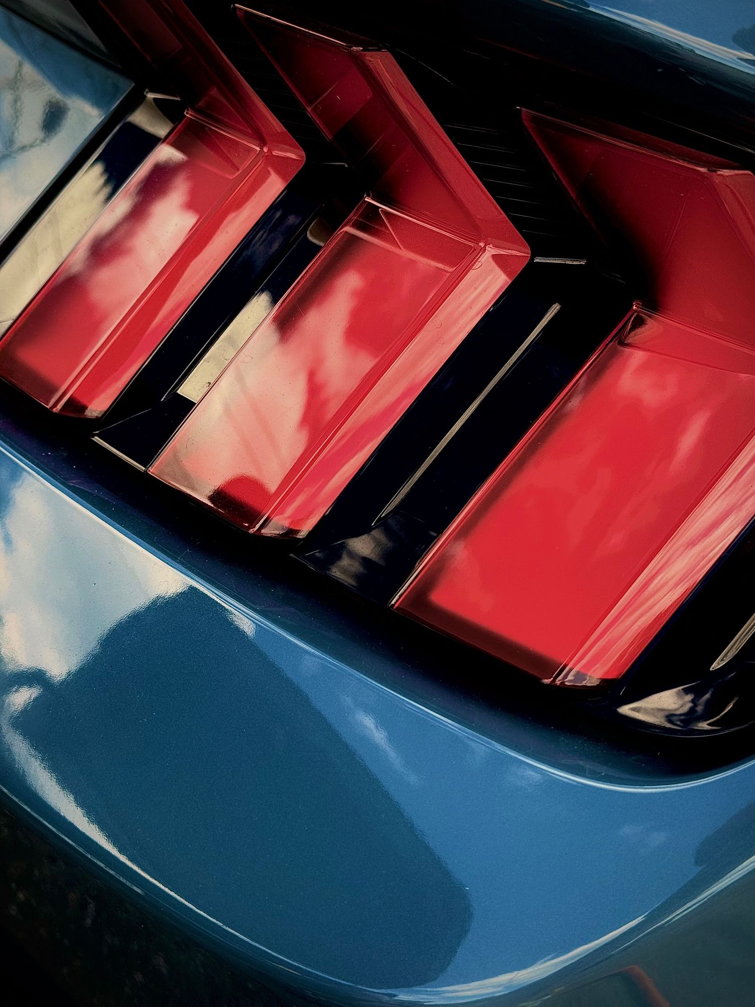 Close-up of a Ford Mustang's distinctive tri-bar sequential LED tail lights in red on a blue car body.