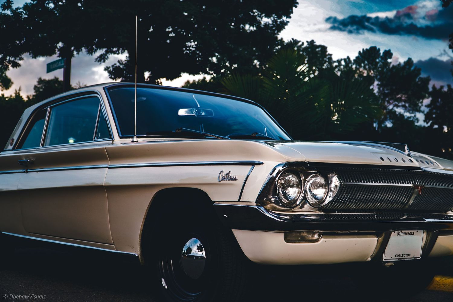 Vintage white 1962 Oldsmobile Cutlass classic car parked outdoors at dusk with dramatic cloudy sky and trees.
