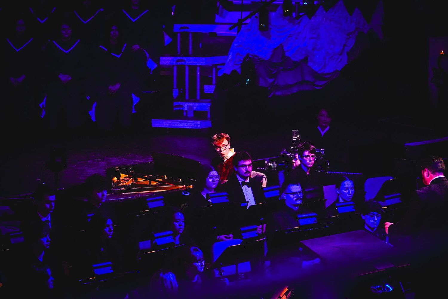 Dark concert hall illuminated by purple and blue stage lights during a performance.