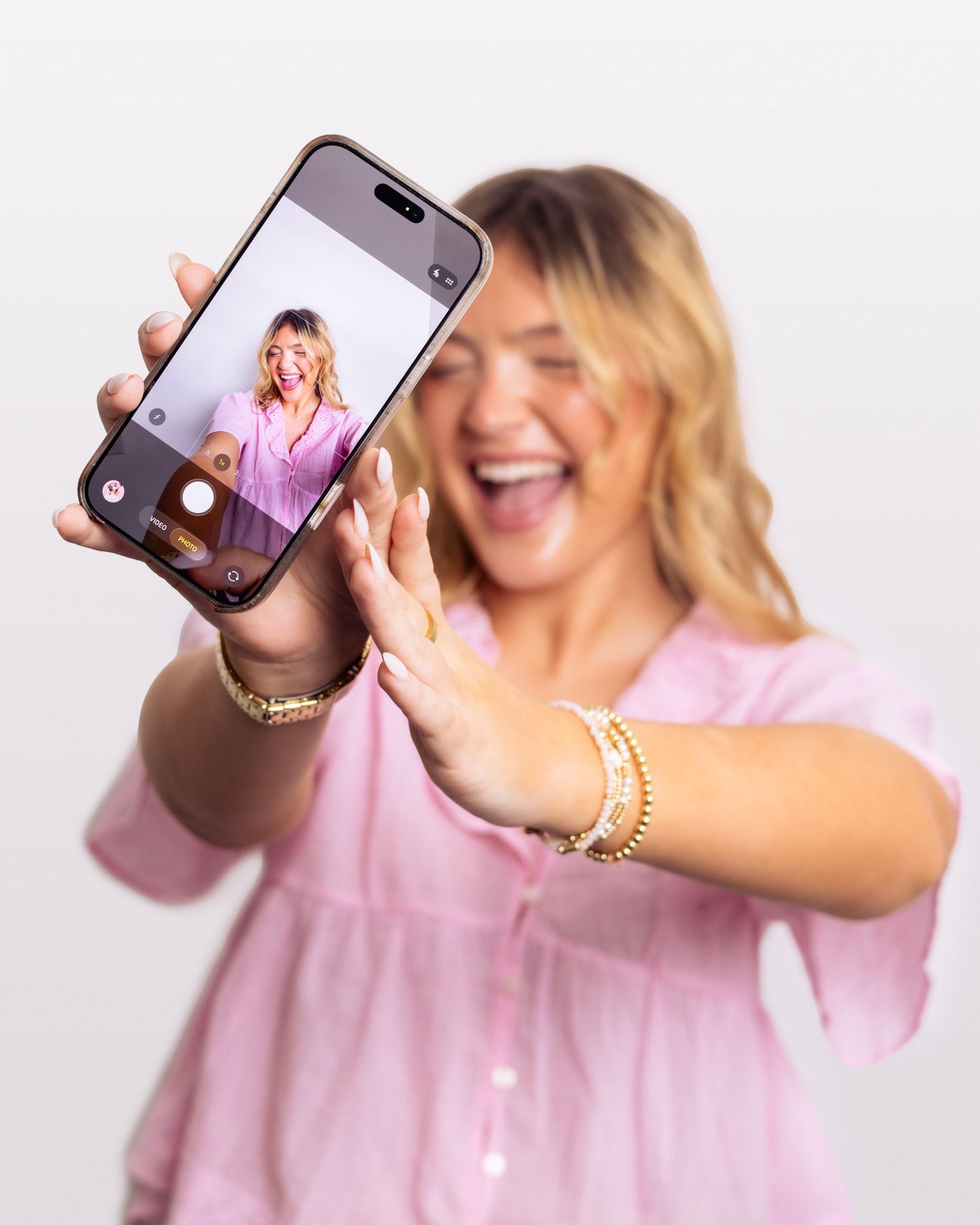 Woman smiling holding a cellphone taking a selfie.