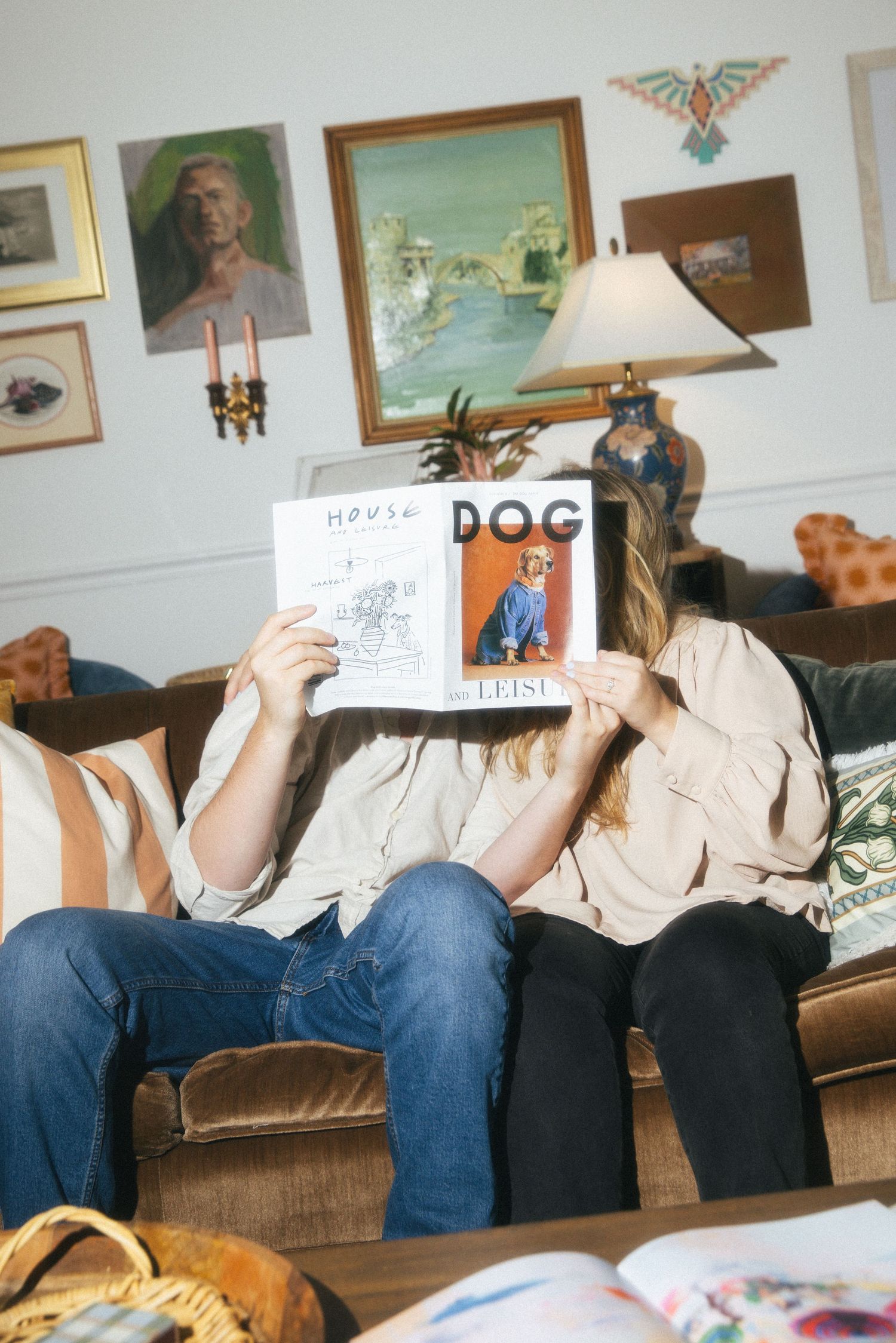 Couple sitting in their living room holding up a magazine covering their faces