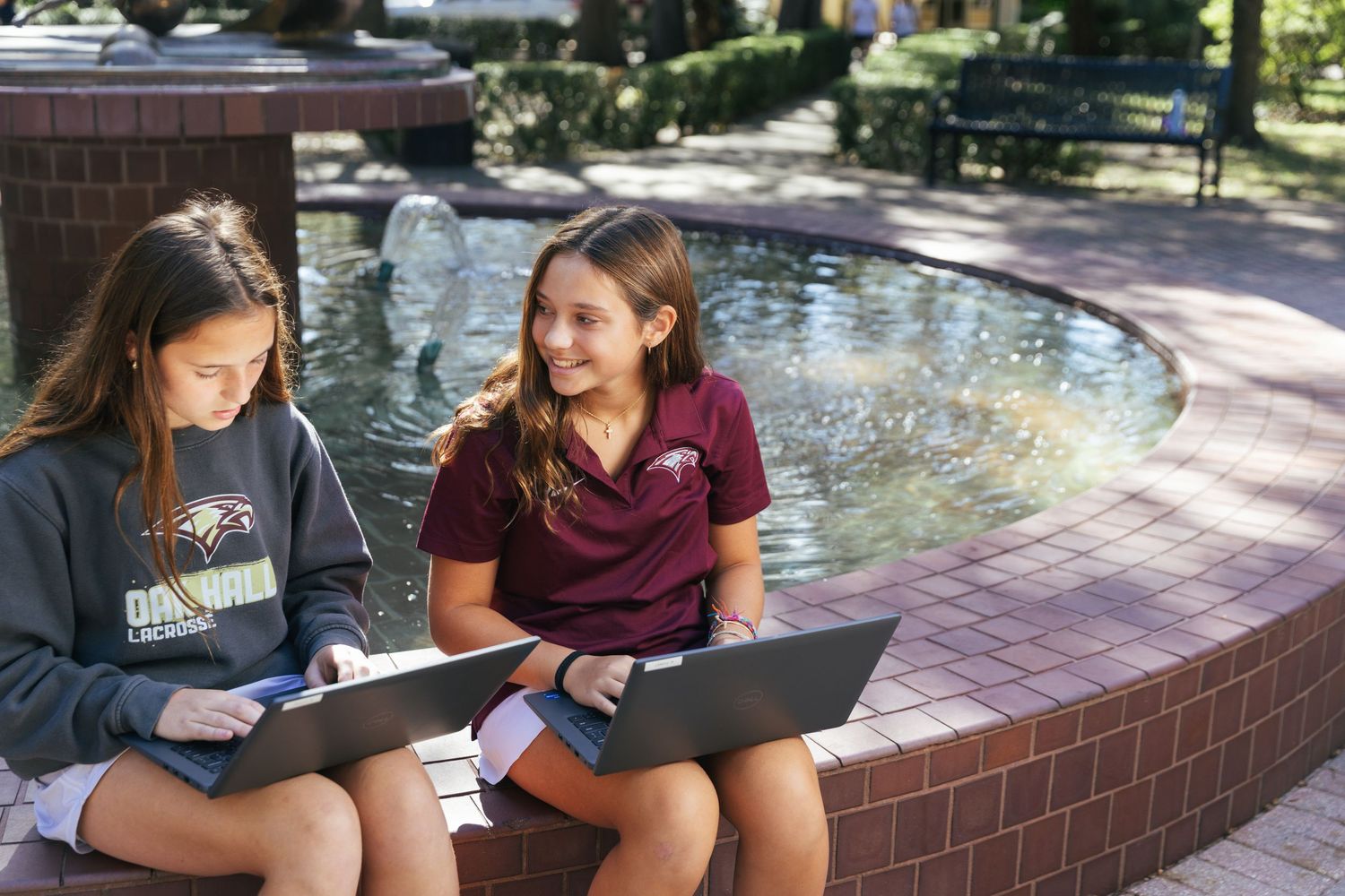 Two female students sitting outside with laptops