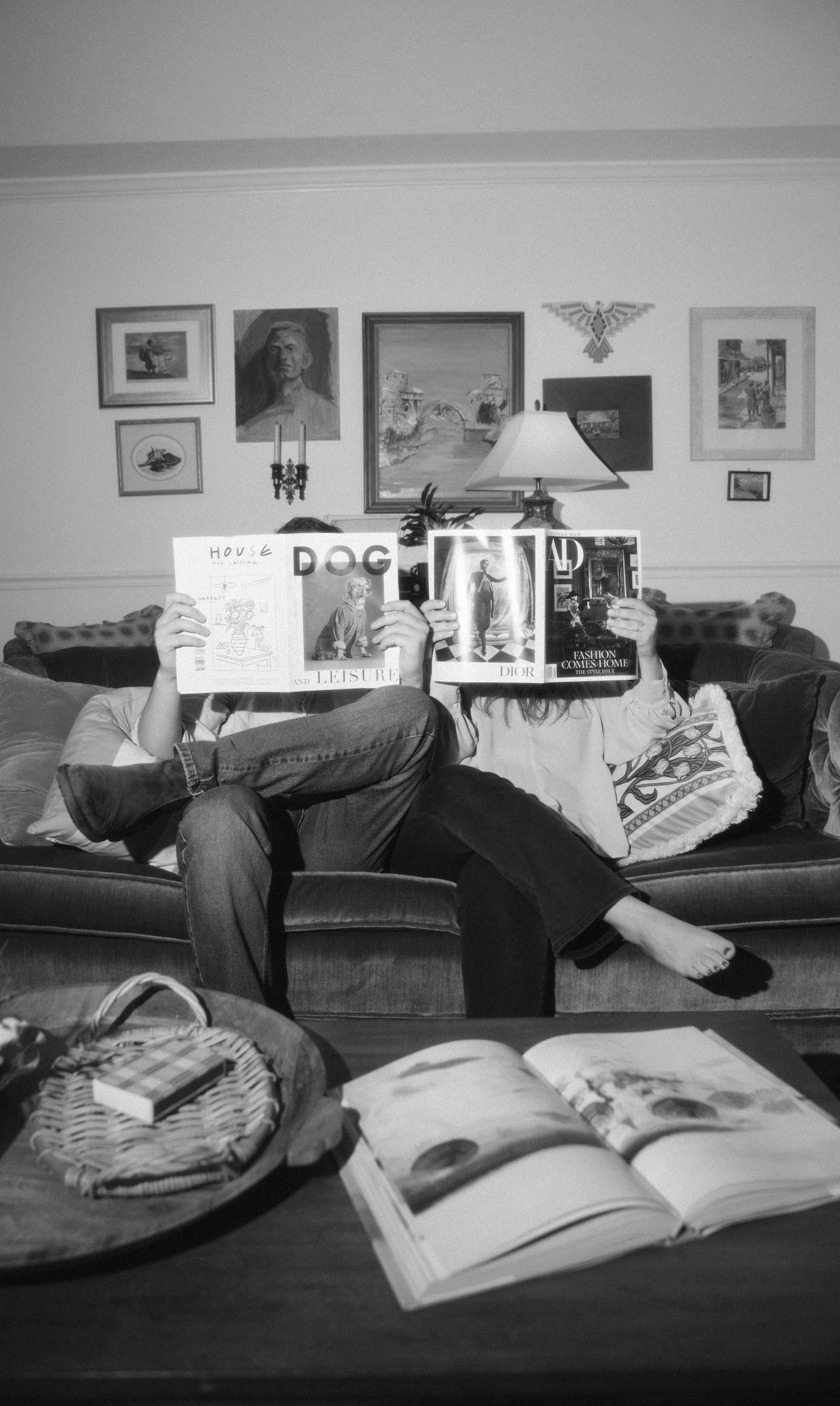 Black and white portrait of a couple sitting in a living room holding up magazines covering their face
