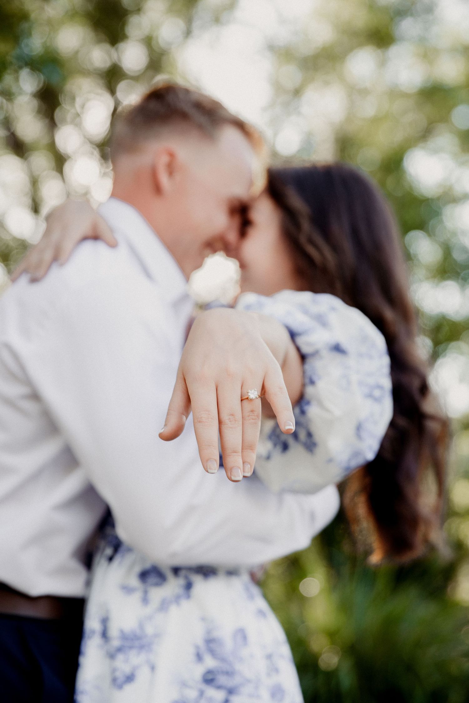 Young couple hugging in an outdoor setting featuring the females engagement ring