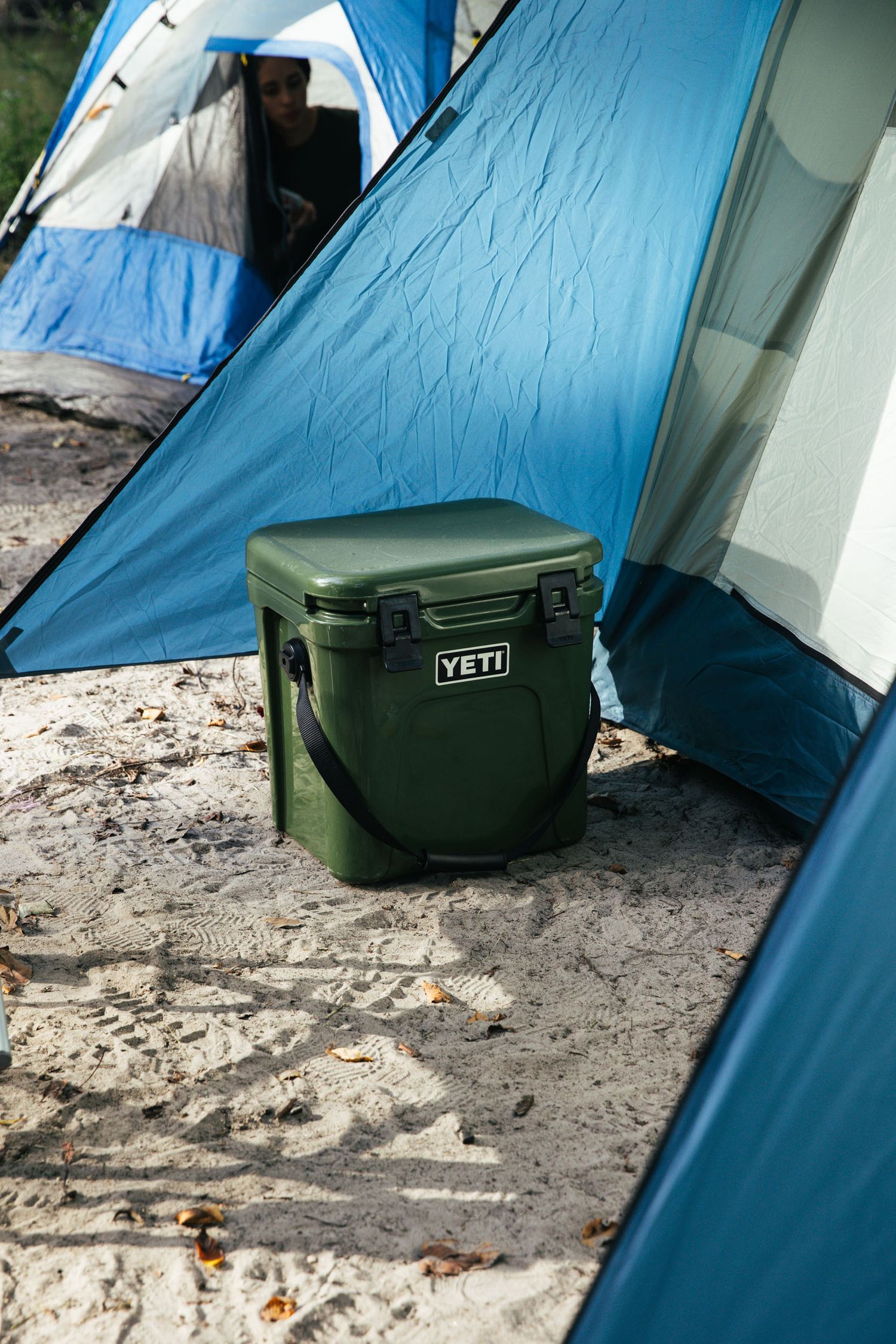 A green yeti cooler sitting by a blue tent