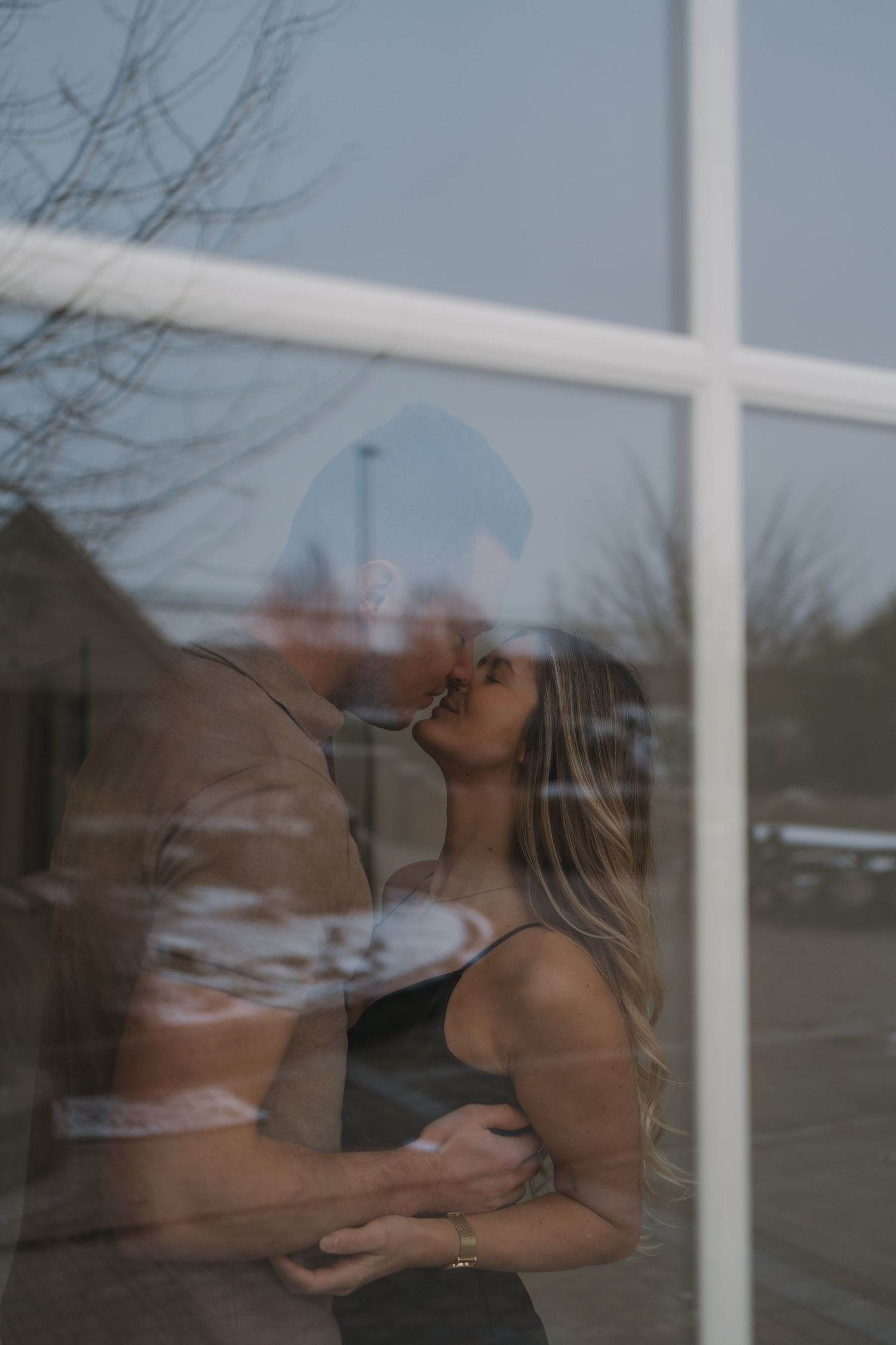Koppel tijdens een koppelshoot, gefotografeerd door een raam voor een creatief effect.