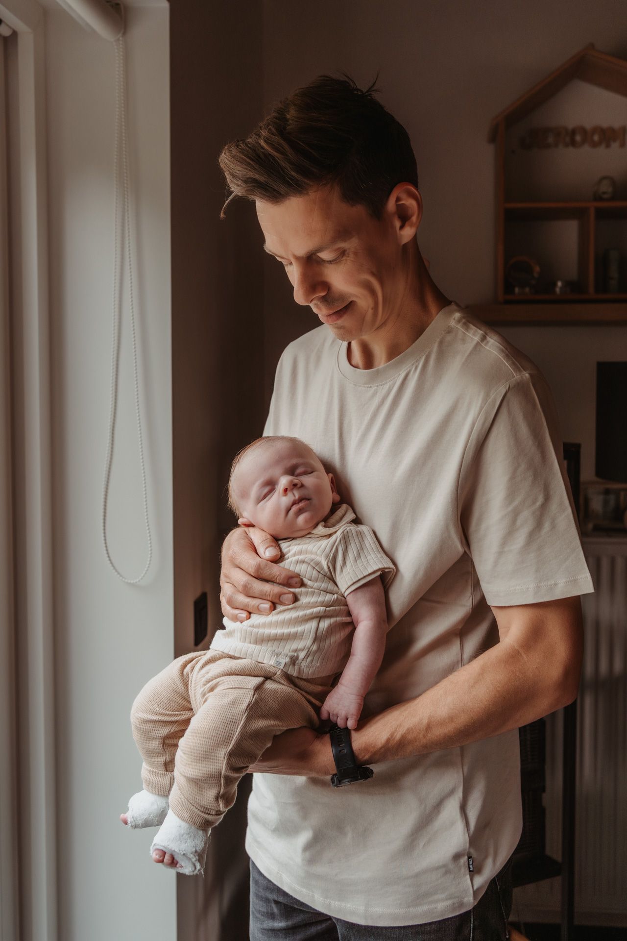 Pasgeboren baby samen met de papa thuis tijdens een newbornshoot.