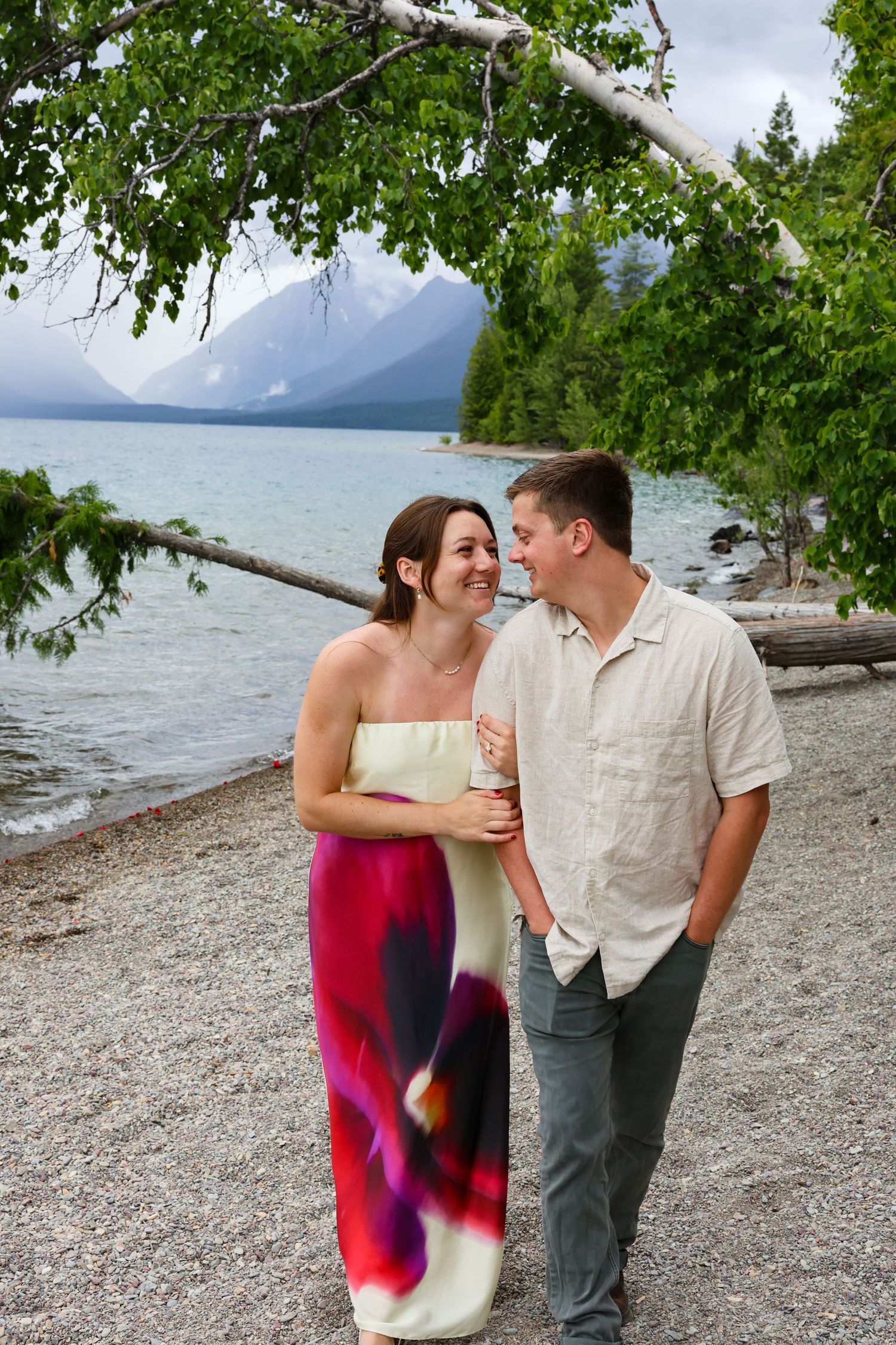 Newly engaged couple walk the beach alongside Lake McDonald in Montana.