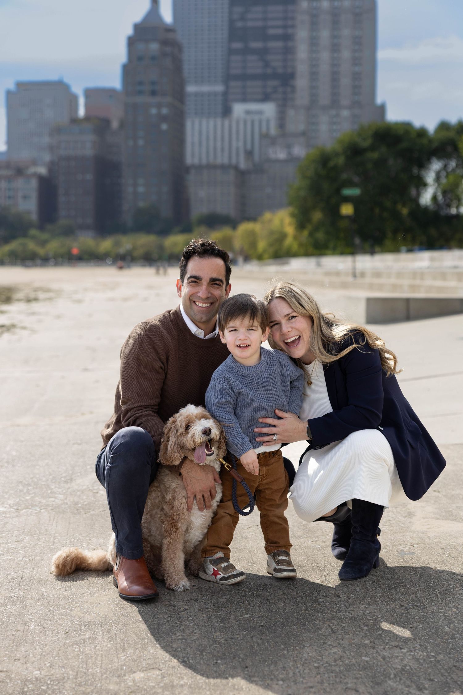 Family of 3 and their golden doodle smile in front of the Chicago skyline.