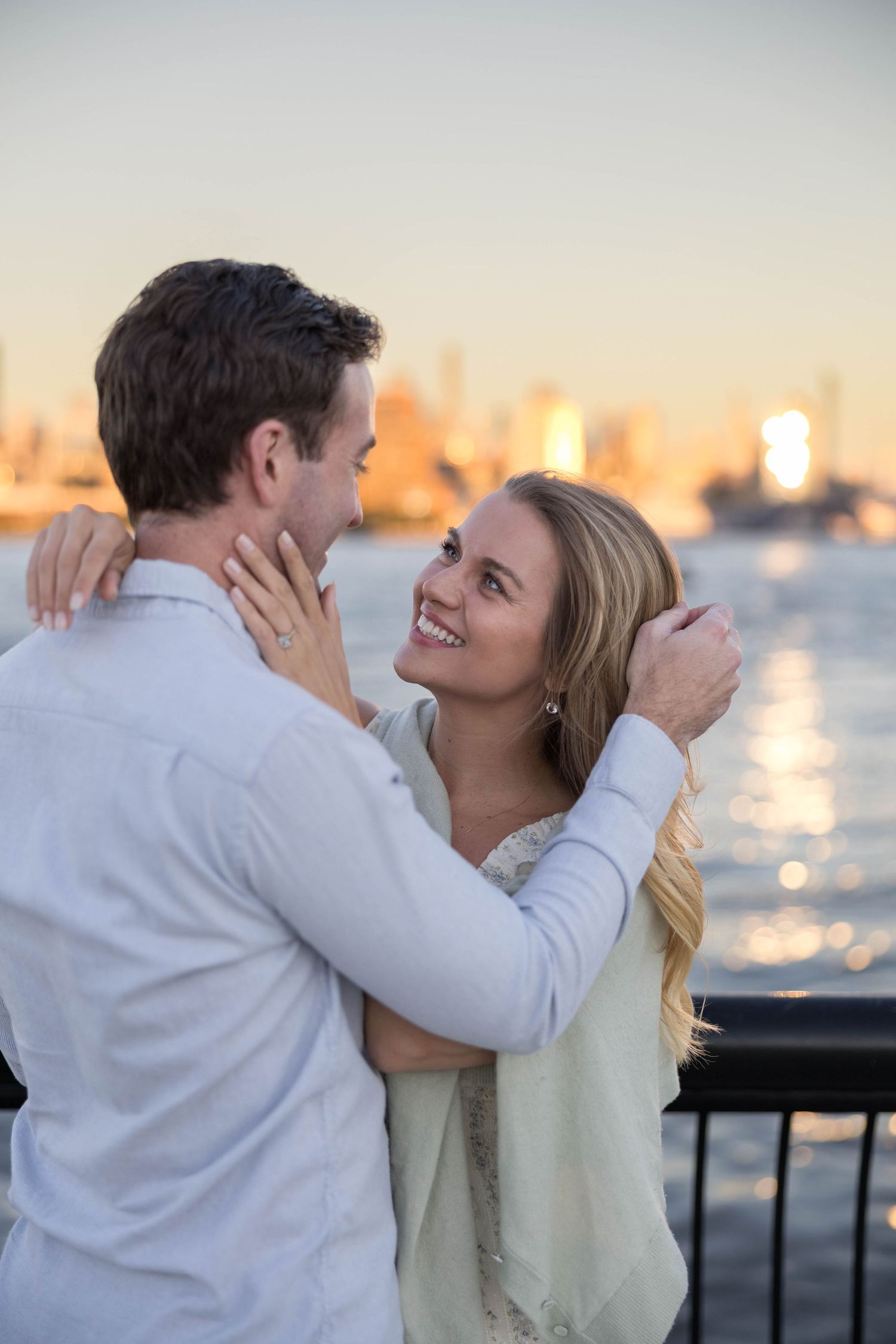 Engaged couple embrace each other in front of New York City skyline.