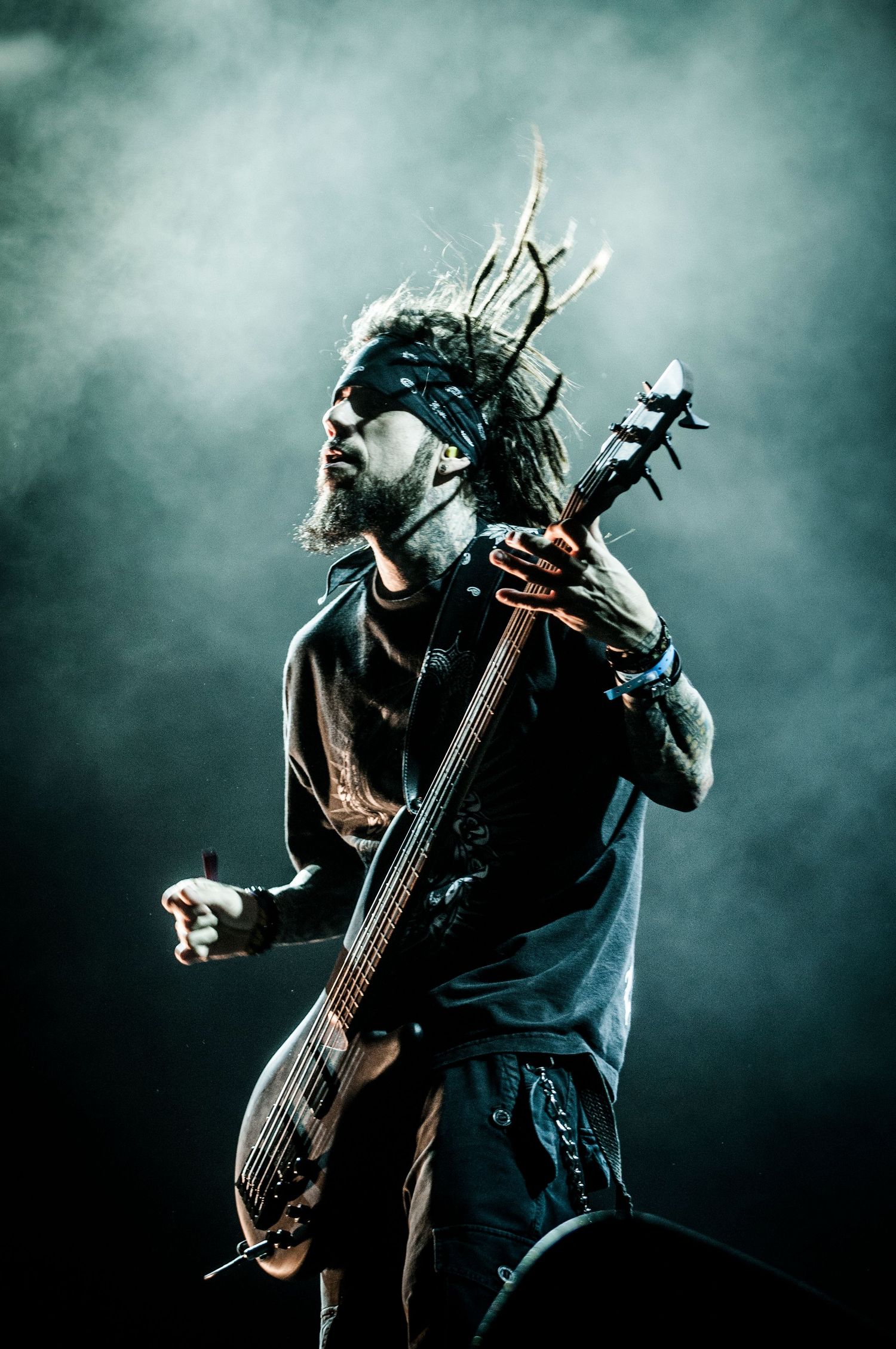 Bass guitarist performing energetically on smoky stage with dramatic teal lighting effects.event photographer in guelph ontario