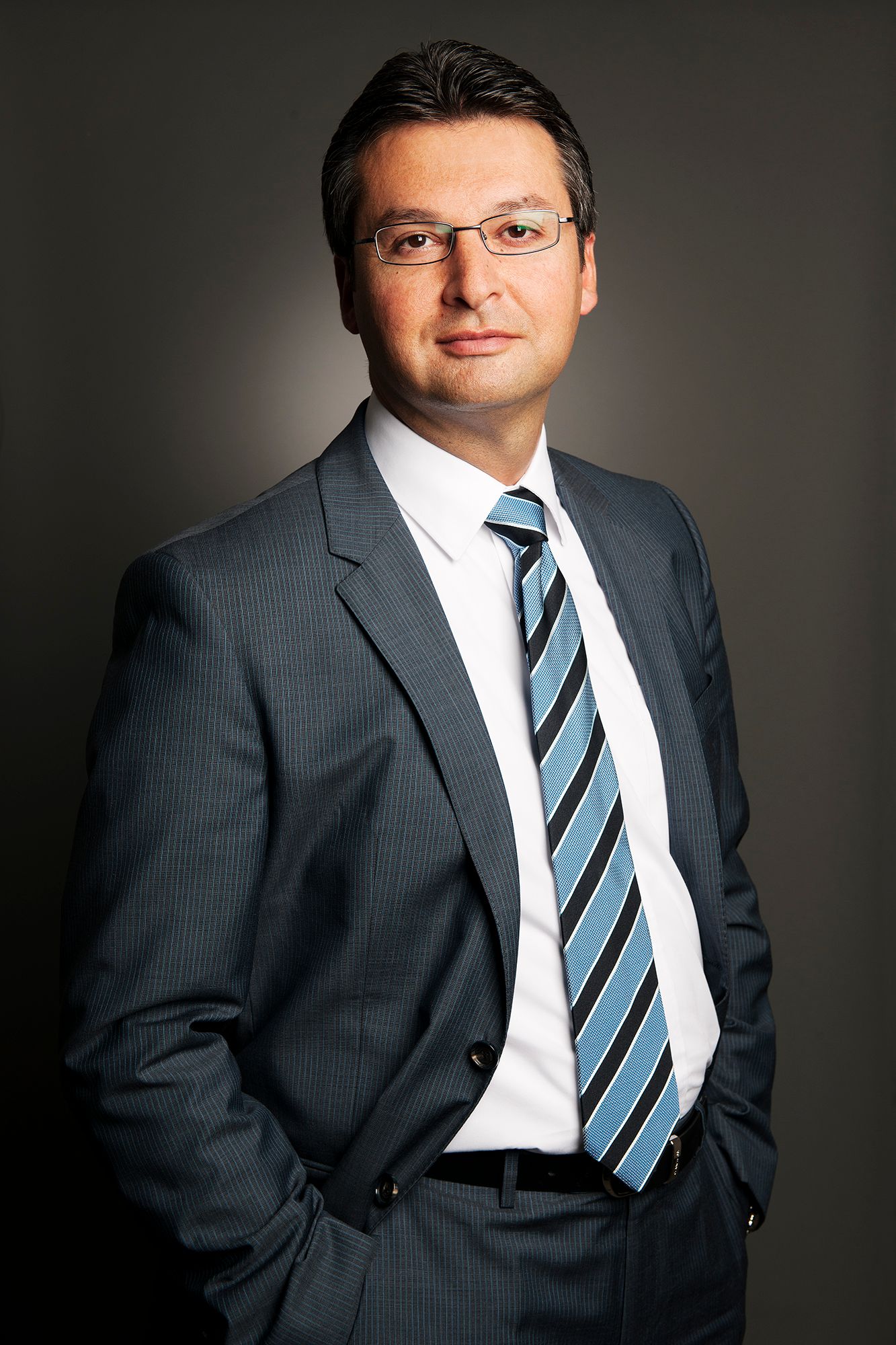 Professional business portrait series in dark grey suit and striped tie against grey backdrop. Commercial Portrait photographer in Ontario