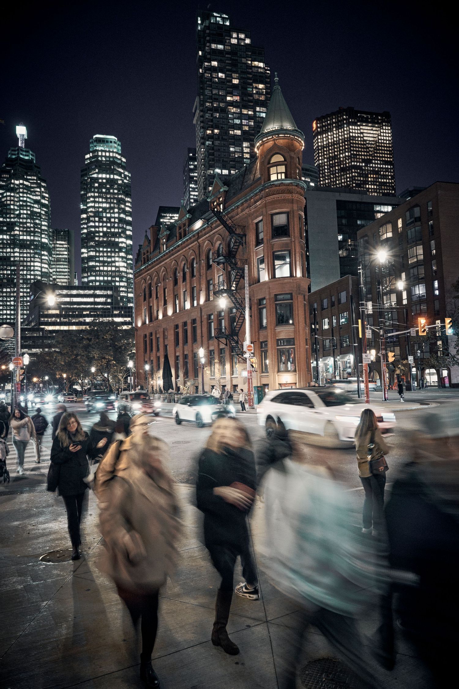 Long exposure cityscape showing motion blur of people walking past illuminated buildings at night in Toronto Ontario Canada.