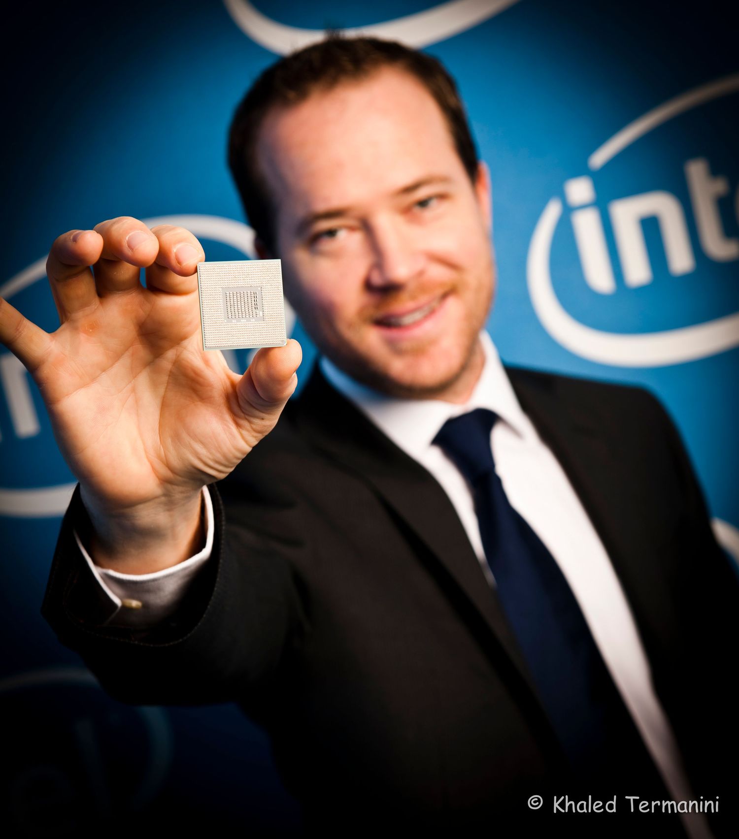 Executive holding computer processor chip against blue backdrop in business attire. Commercial Portrait photographer in Ontario