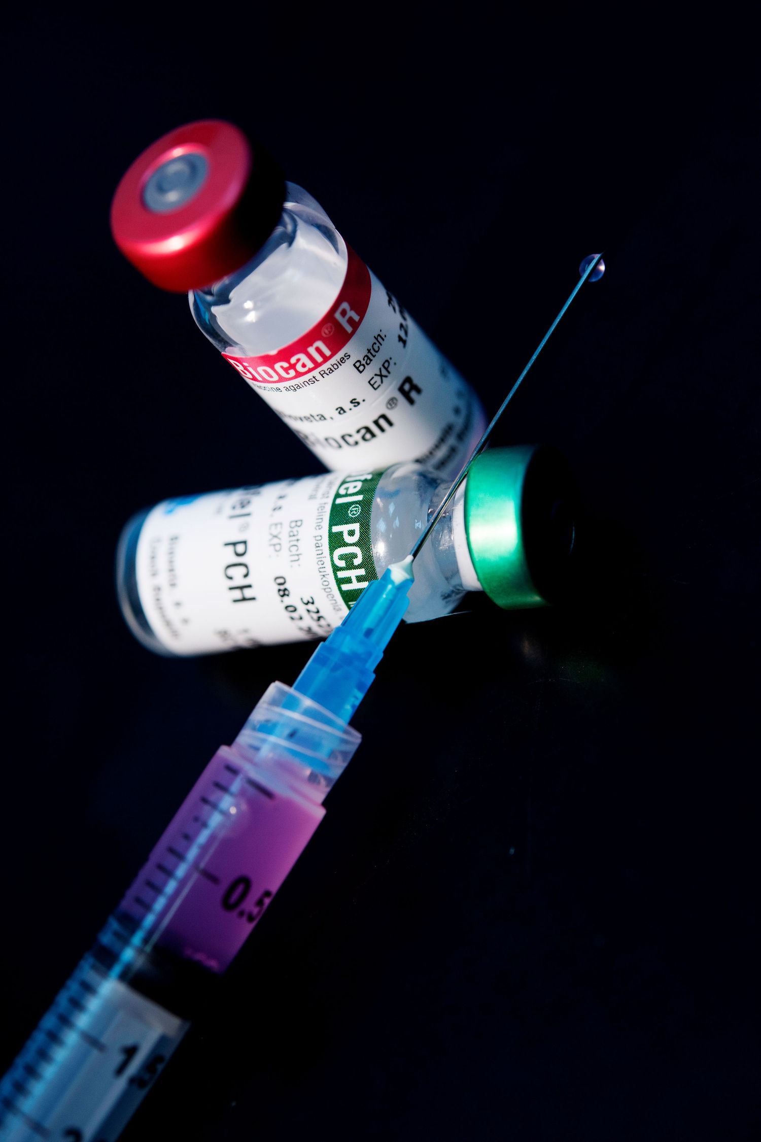 Medical vials and syringes arranged in artistic lighting against dark background.