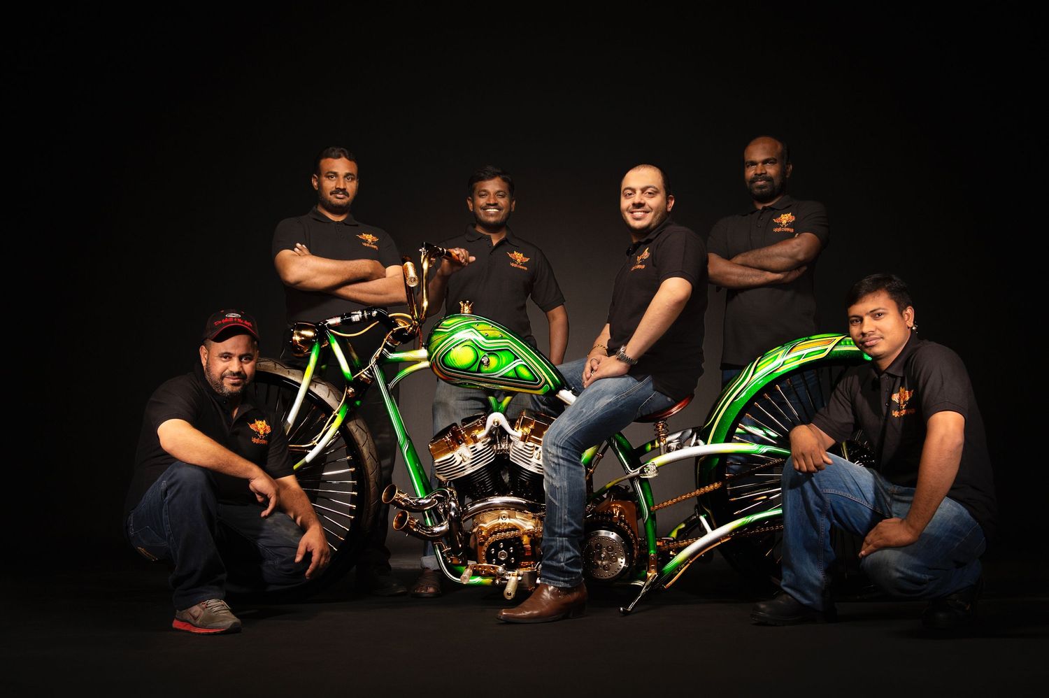 Group photo of motorcycle enthusiasts posing with custom green bikes against dark background.
