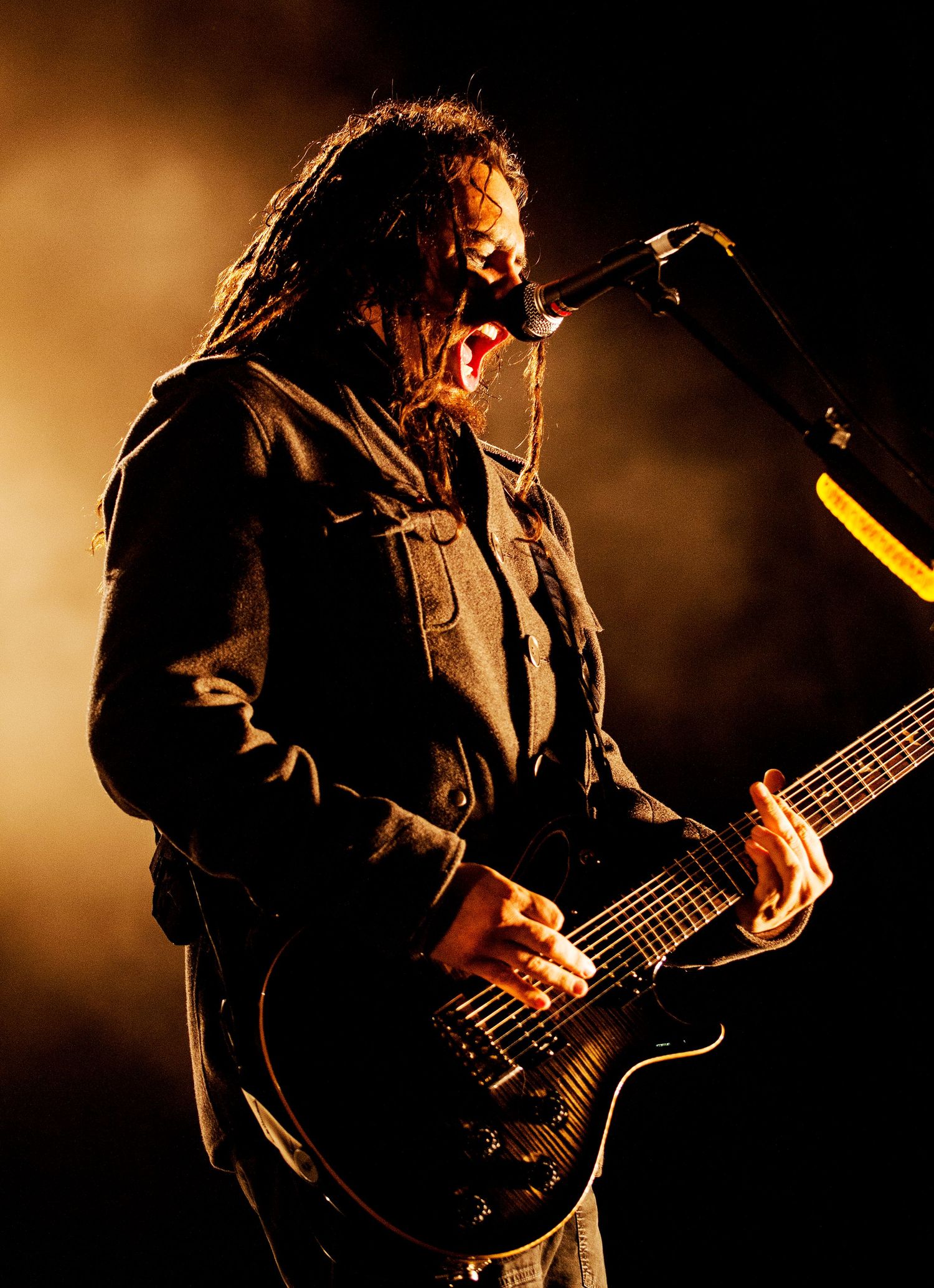 Silhouetted guitarist playing in dramatic sepia-toned lighting on dark stage. Munki is the guitarist from Korn
